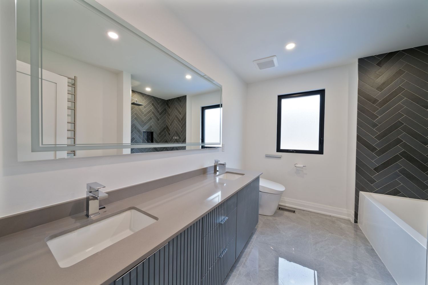 Modern bathroom interior with herringbone pattern wall tiles, white countertop, and gray vanity cabinet in neutral tones.