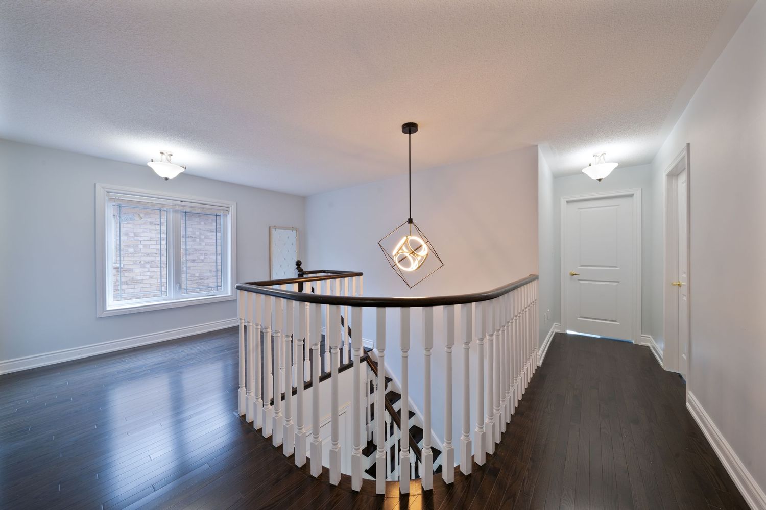 Modern staircase with white walls and dark hardwood flooring features elegant chandelier lighting and curved railing details.