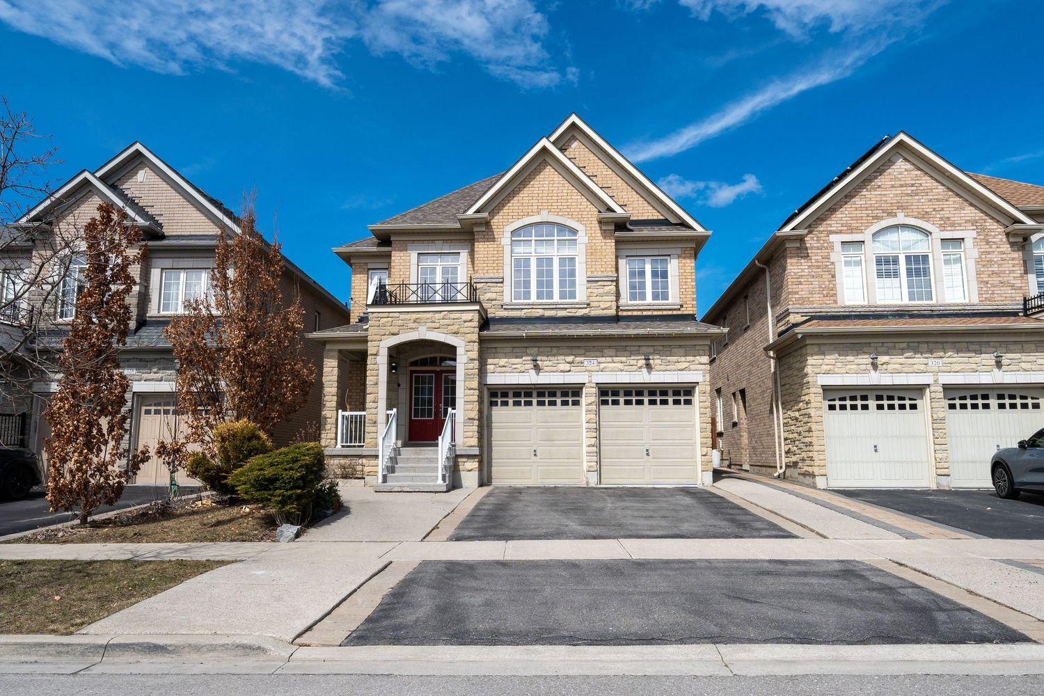 Modern beige suburban house with double garage and sloped driveway against blue sky with wispy clouds.