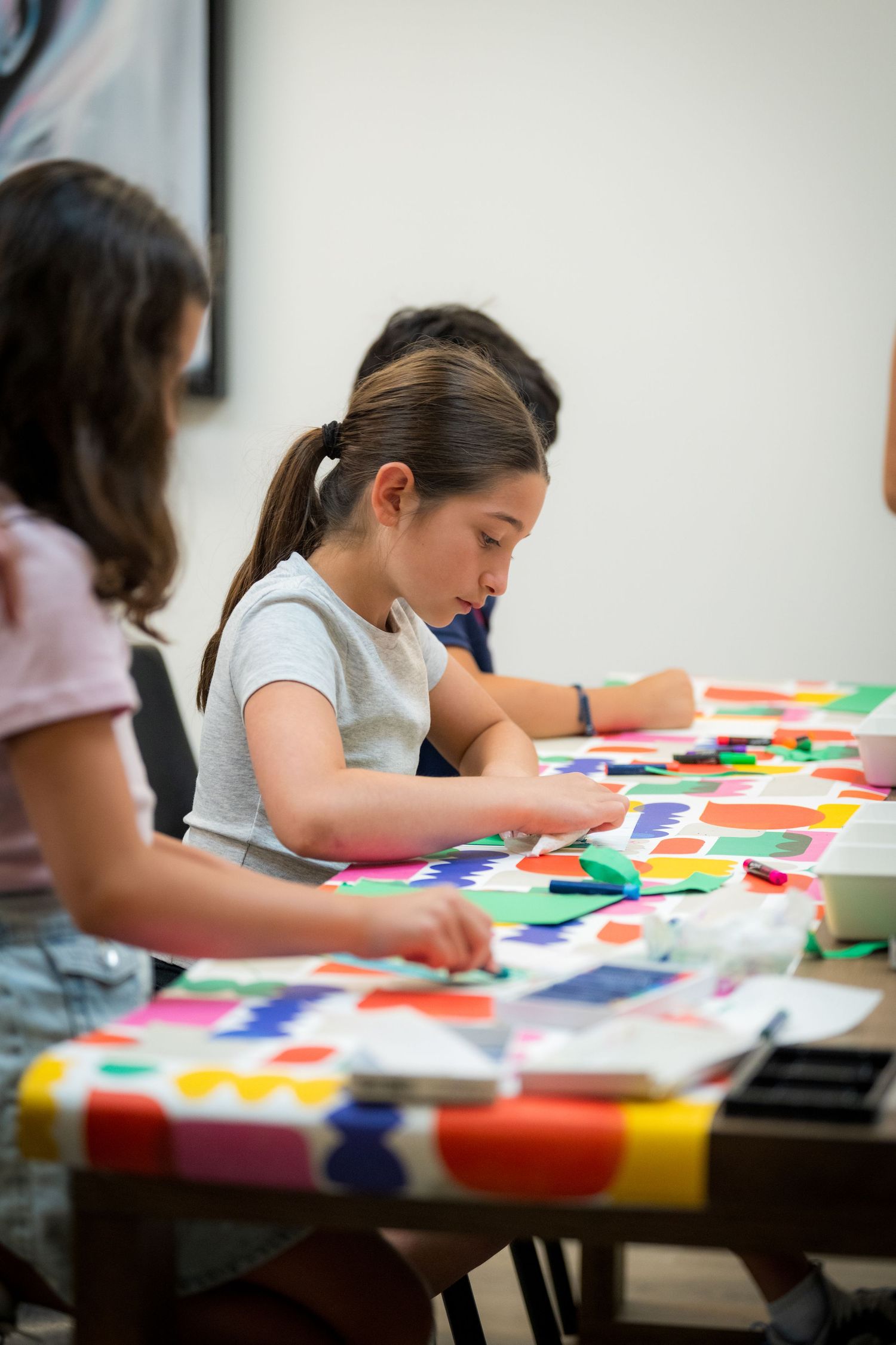 Young girl carefully works on a colorful paper collage at a bright art table.