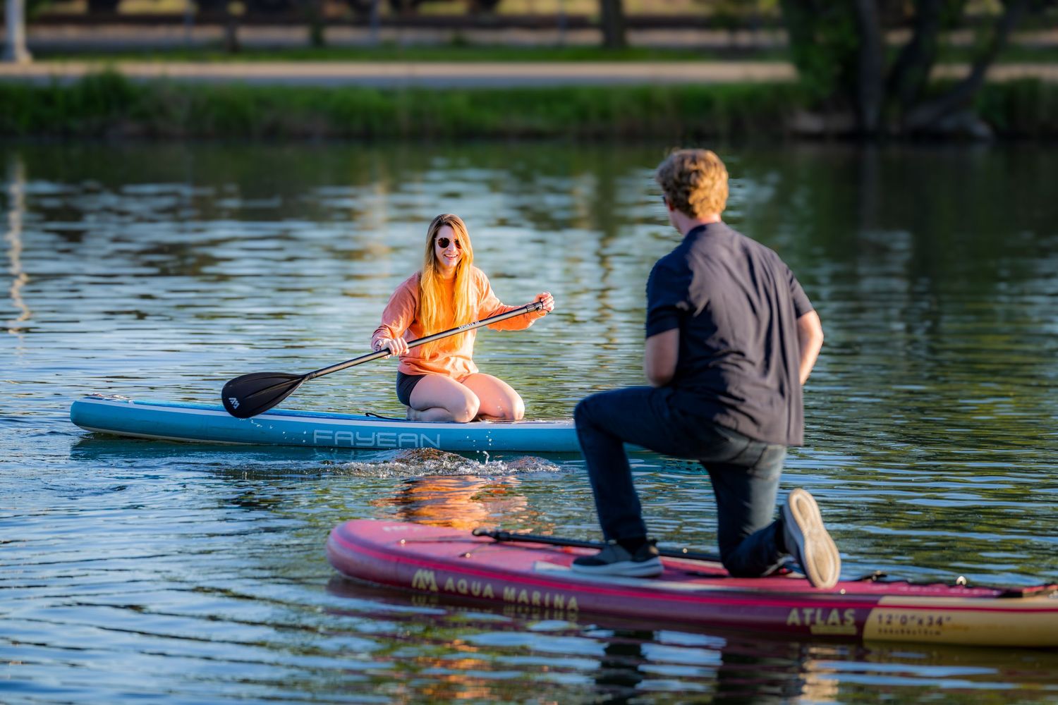 Couple paddleboarding on a calm lake during a sunny day.