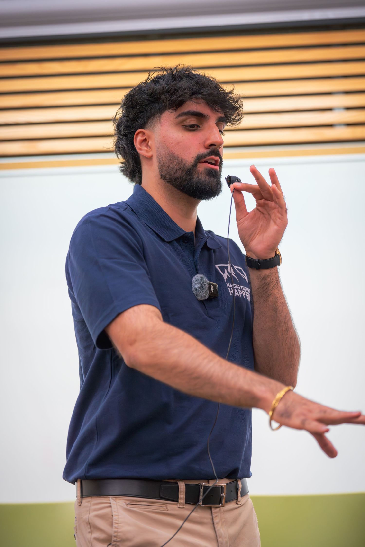 Speaker in navy polo shirt gesturing while giving presentation in conference room.
