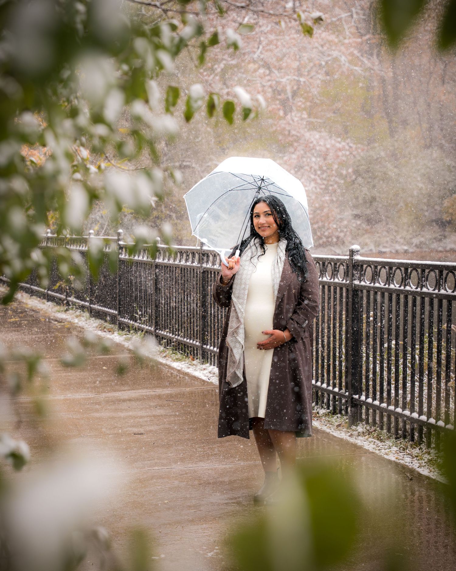 A person in a dark coat holds a white umbrella while walking along a railing-lined path in autumn.