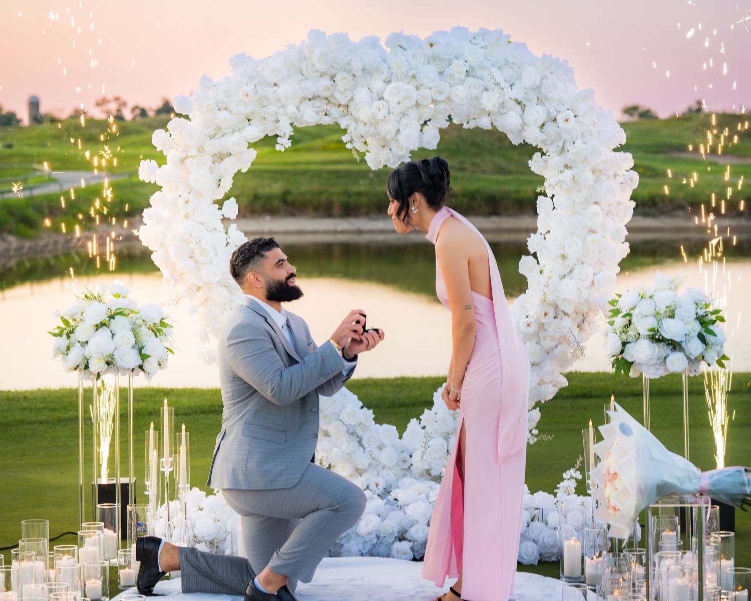Beautiful proposal setup with white floral arch and candles at sunset.