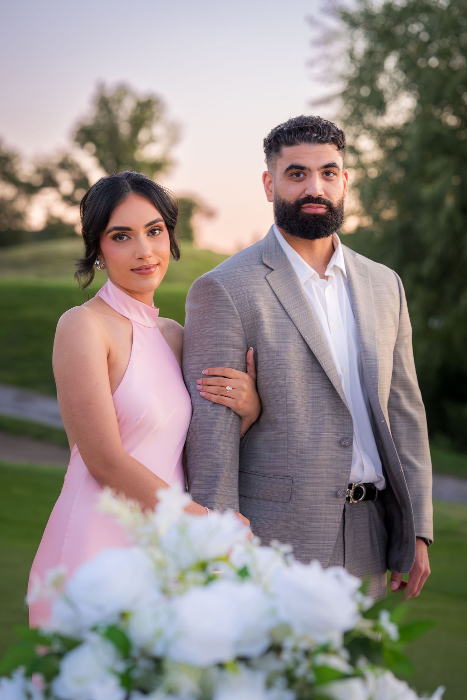 A couple stands close together with ethereal white smoke effects in an outdoor setting at sunset.