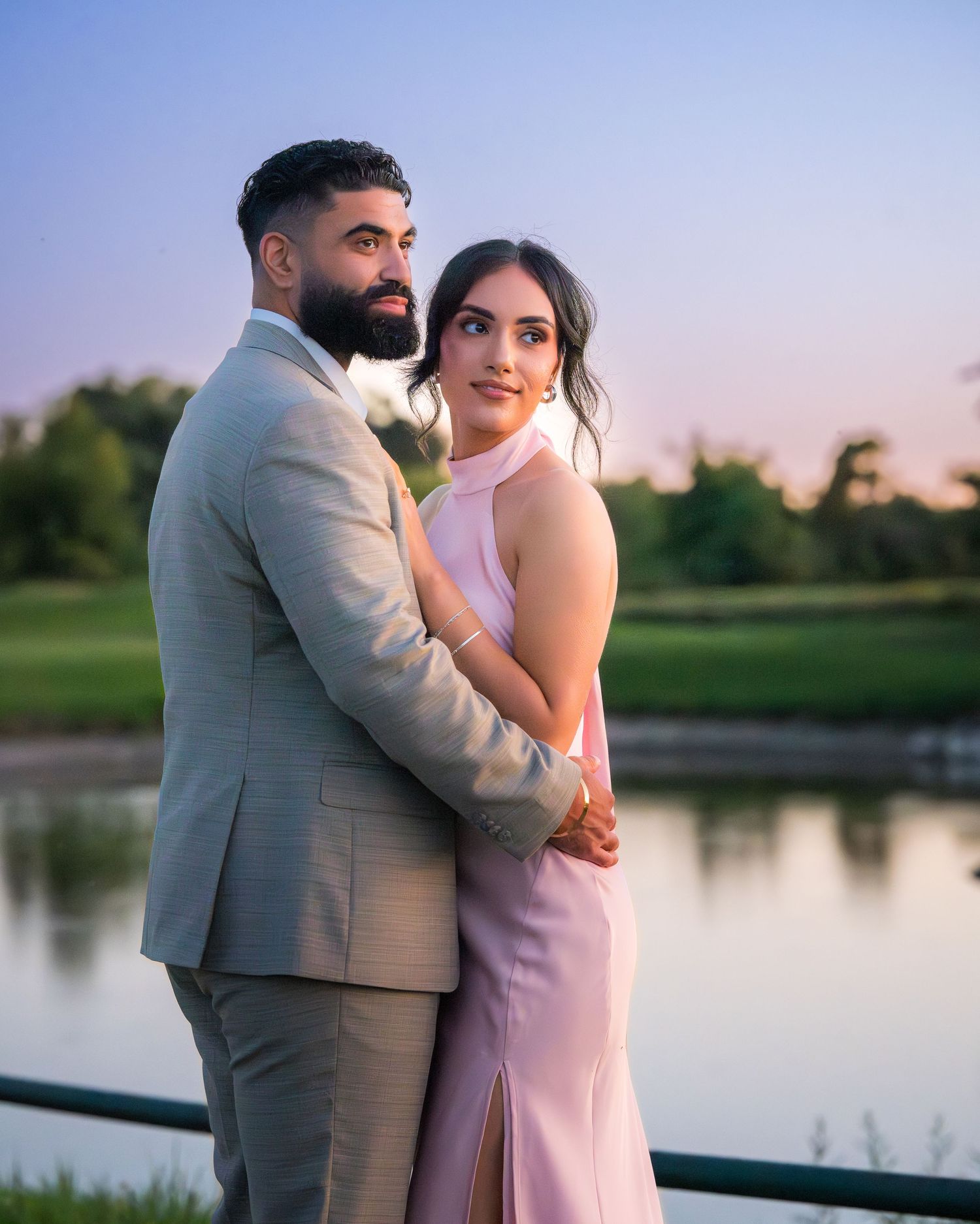 Elegant couple shares romantic moment by lake during sunset photo session.