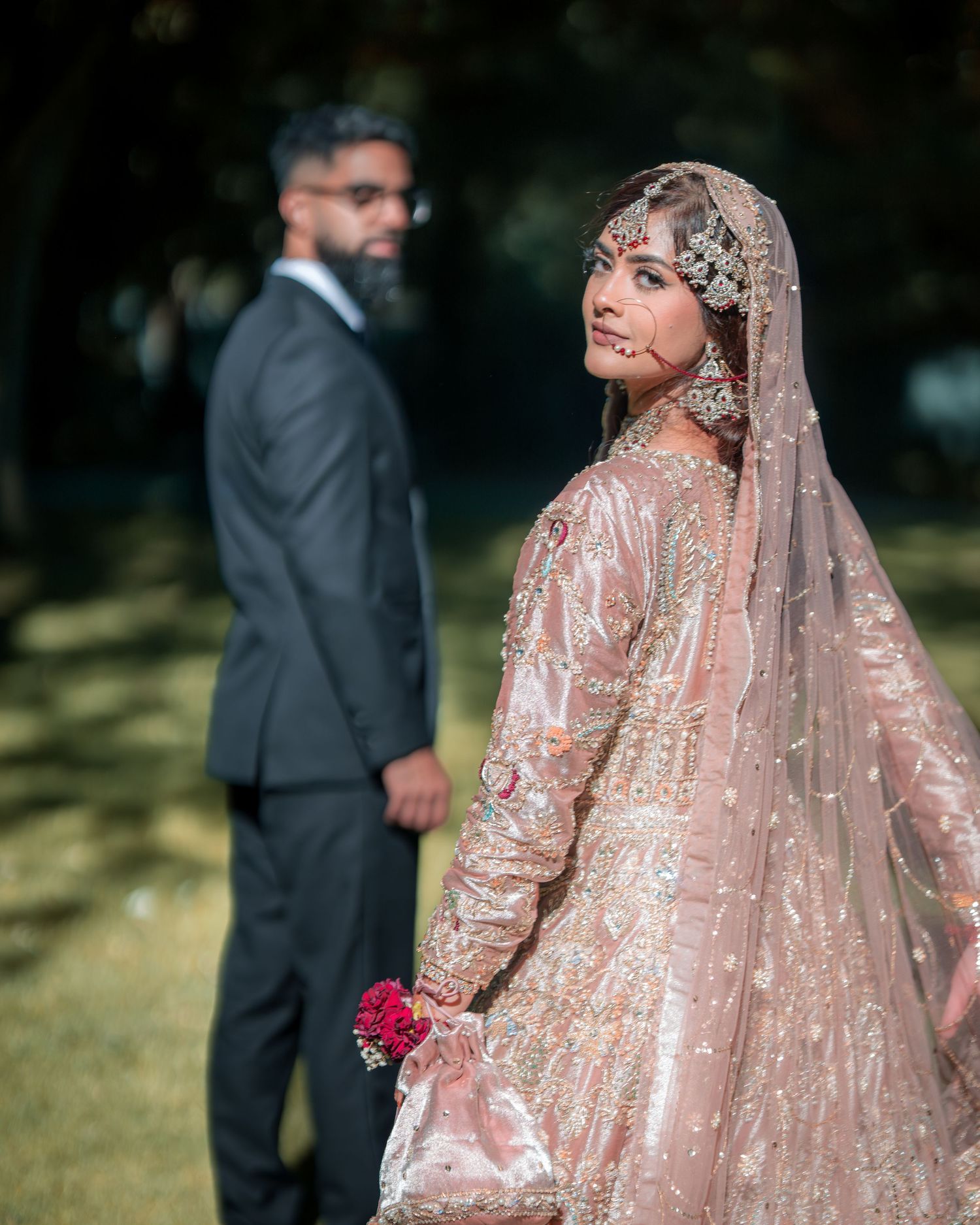 Wedding couple poses outdoors in traditional South Asian attire with bride in pink embroidered lehenga.