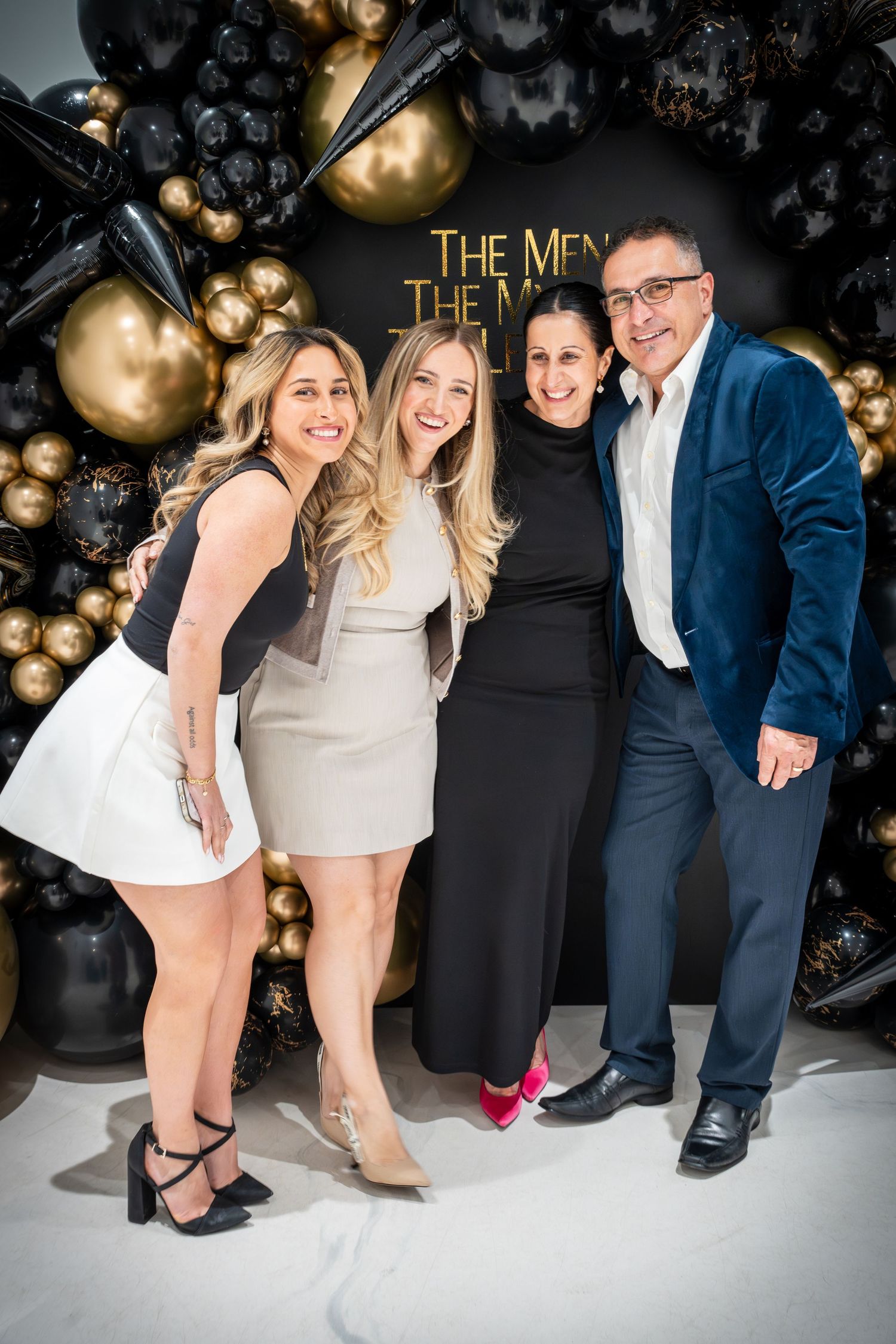 Stylish partygoers showing off their shoes and outfits against black backdrop with gold balloons.