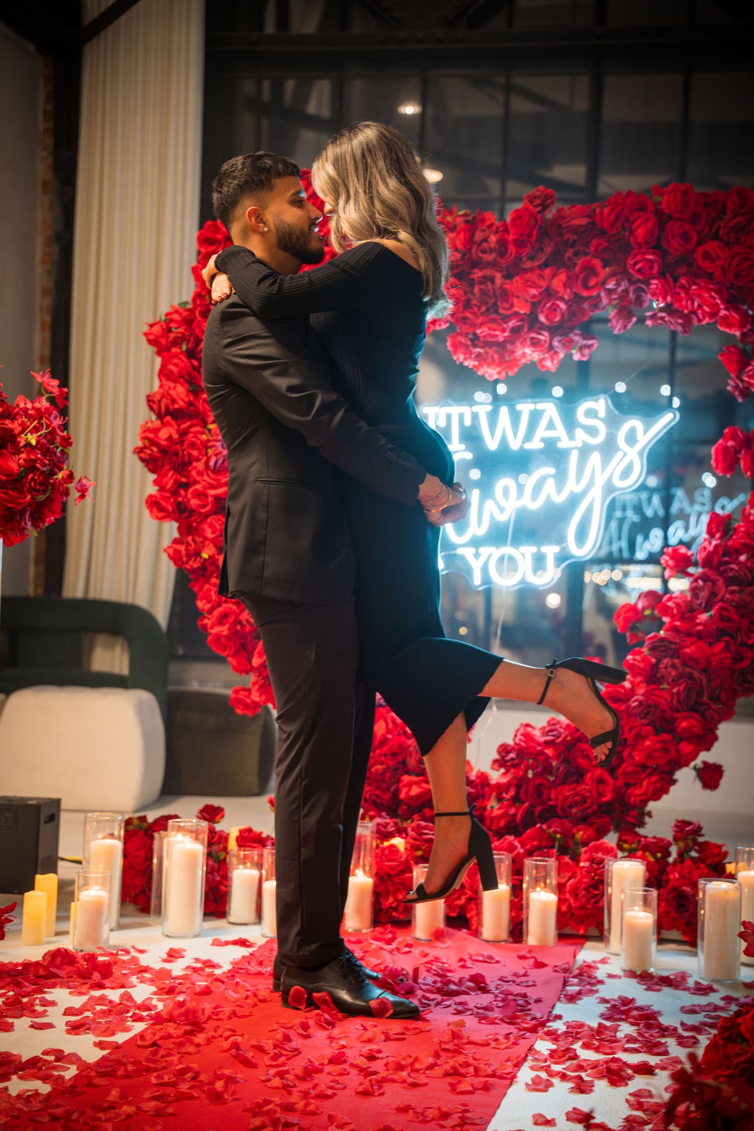 Couple sharing intimate moment surrounded by red roses and glowing neon signage.