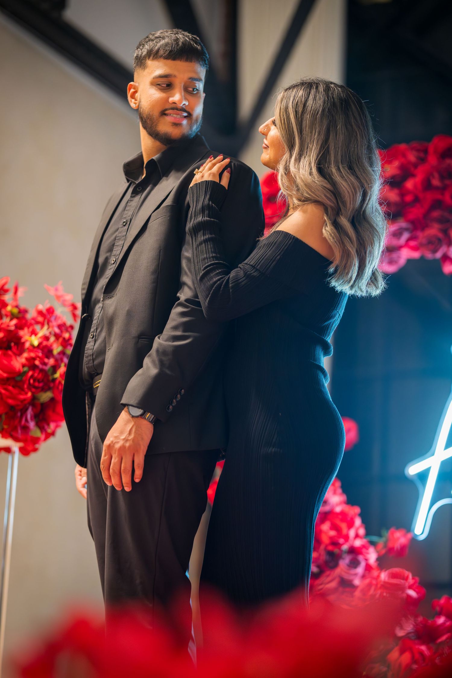 Couple shares an intimate moment in front of red roses and blue neon lighting.