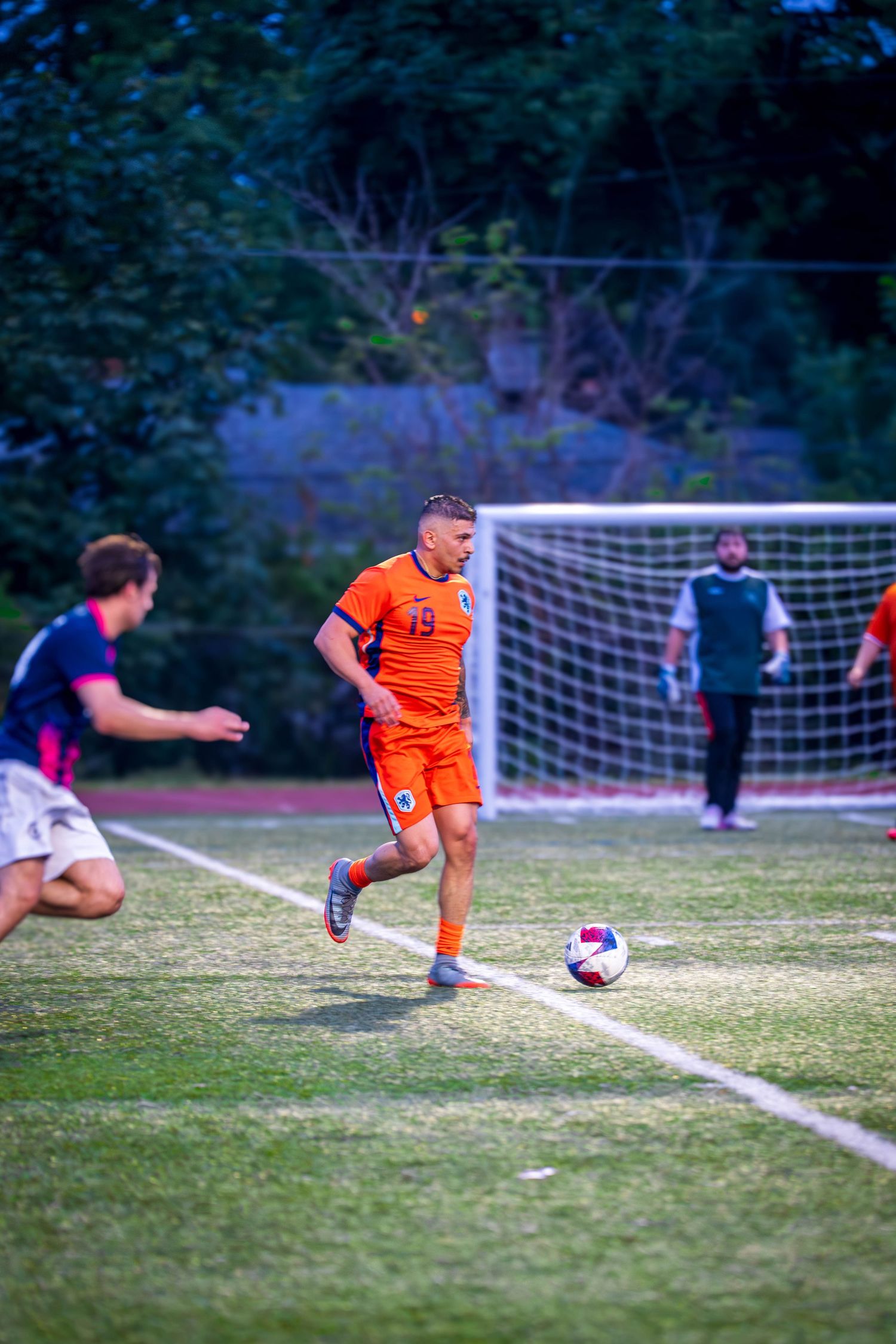 Player in orange jersey prepares to kick soccer ball near goal during match.