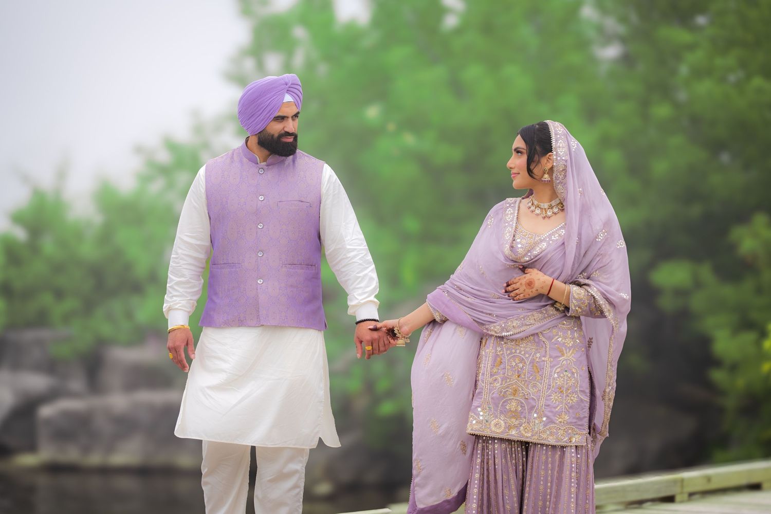 A couple in matching lavender traditional attire holding hands during an outdoor photoshoot.