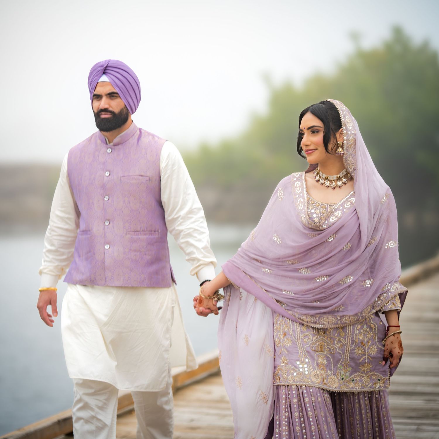 Couple in coordinating purple and white Indian formal wear photographed by a waterfront.