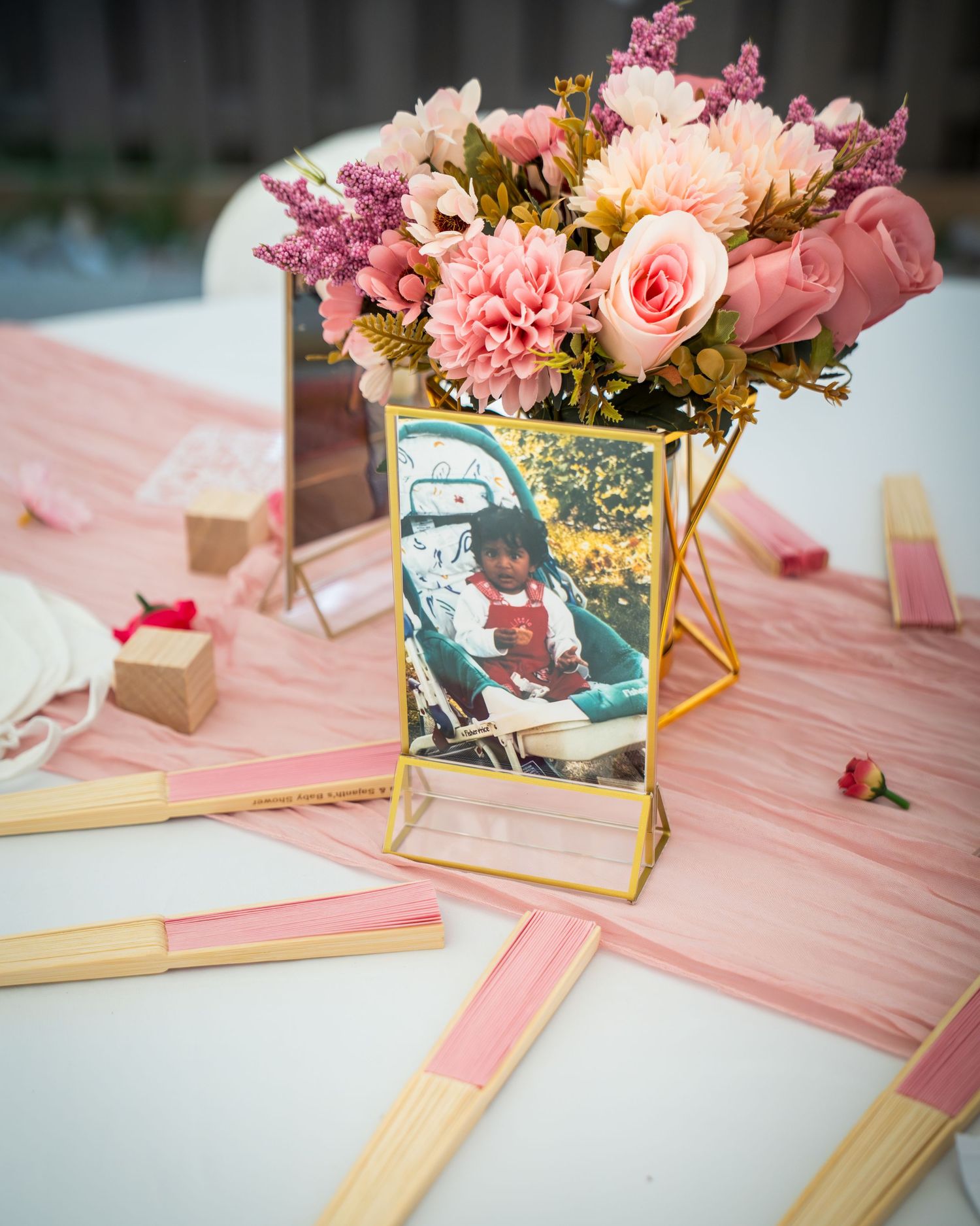 Pink and gold floral table decorations with framed photos at a baby shower.