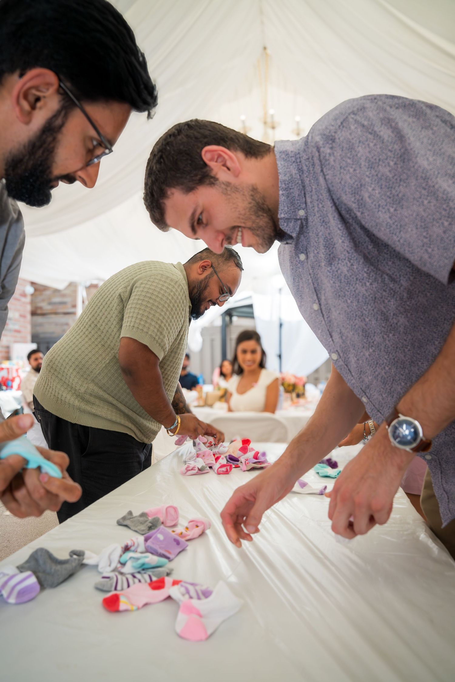 People leaning over a table arranging small pink and gray decorative elements at an event.