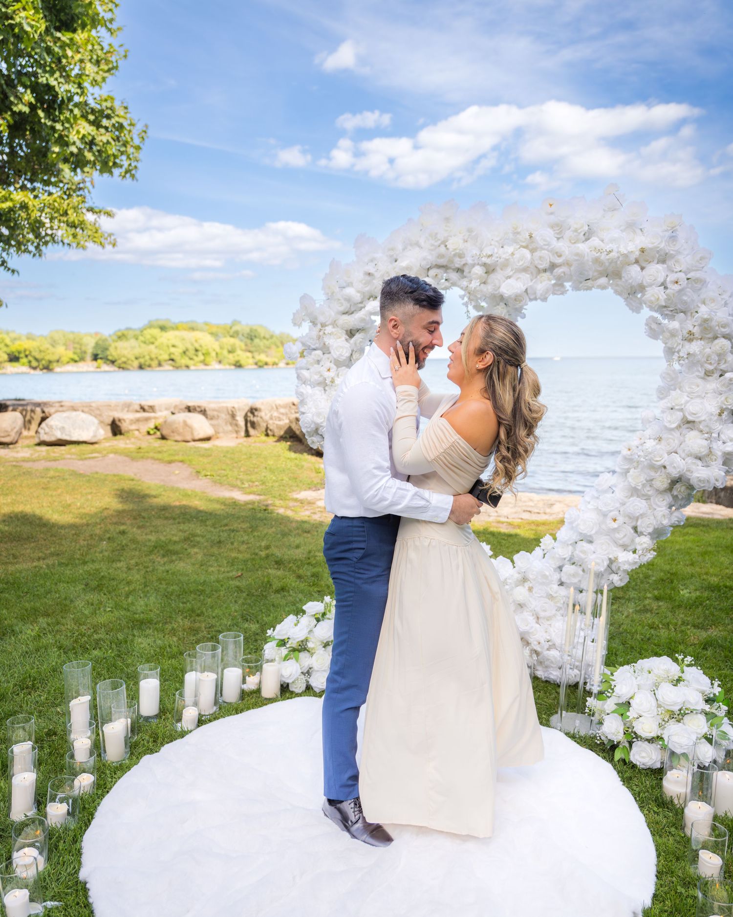 Oceanfront proposal setup with white floral arch and romantic candle-lined walkway.