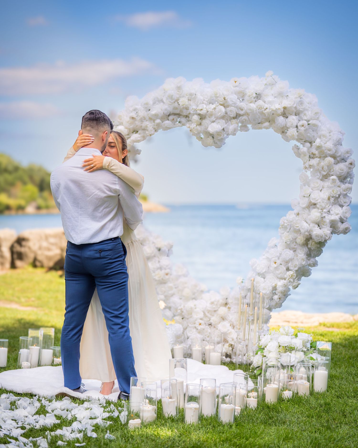 Wedding ceremony site decorated with white floral arch and candles overlooking the ocean.