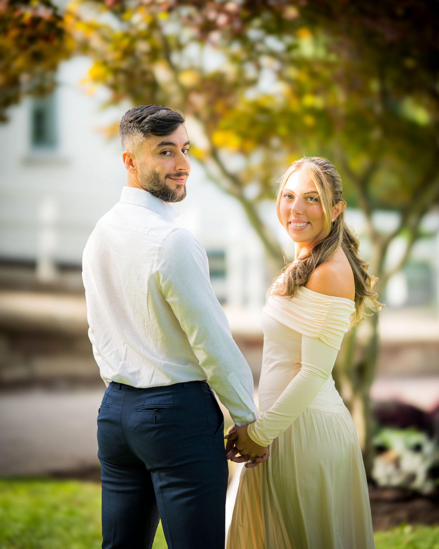 Joyful couple in formal attire sharing playful moments in outdoor garden setting.