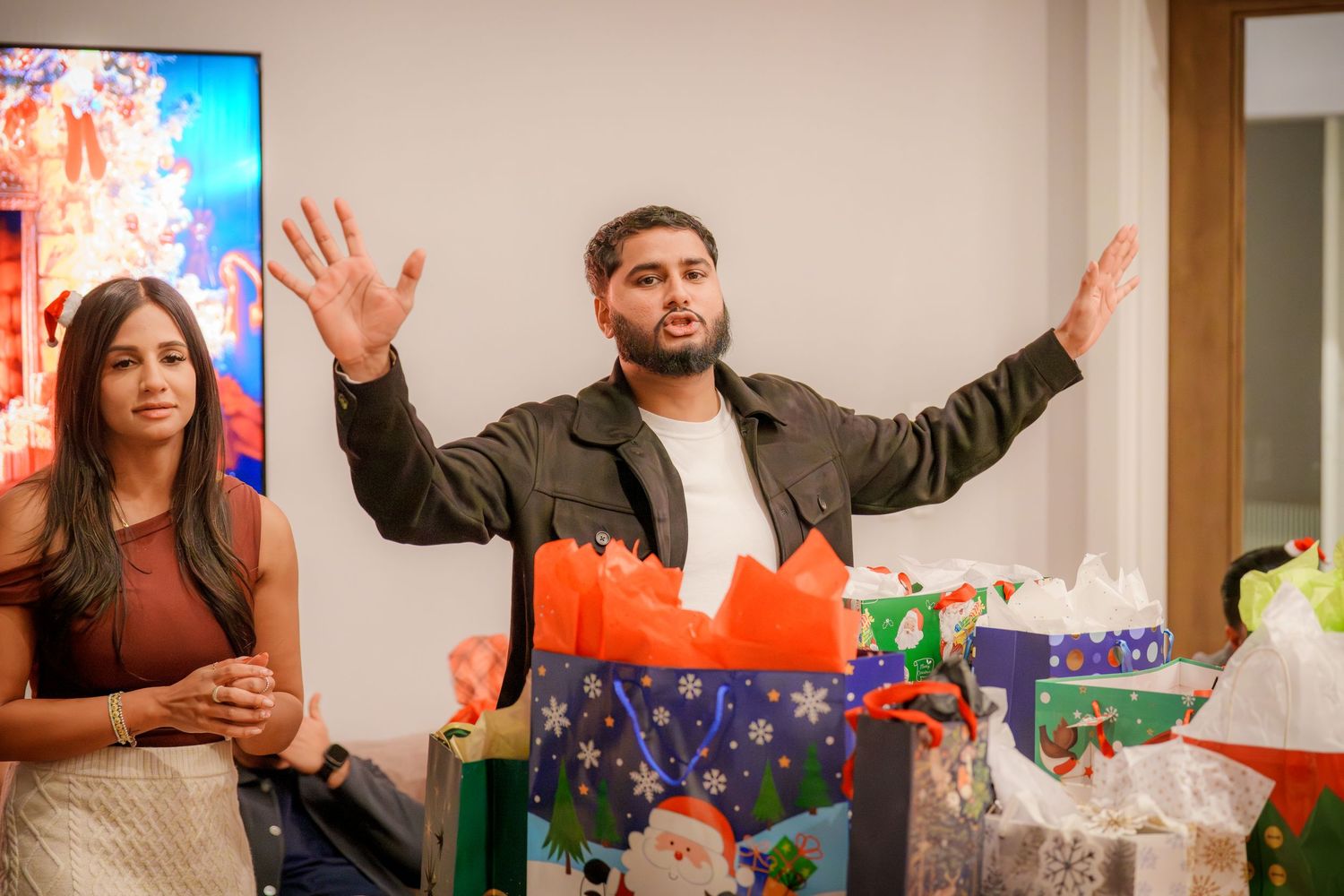 People celebrating with animated gestures in front of a bright TV display.