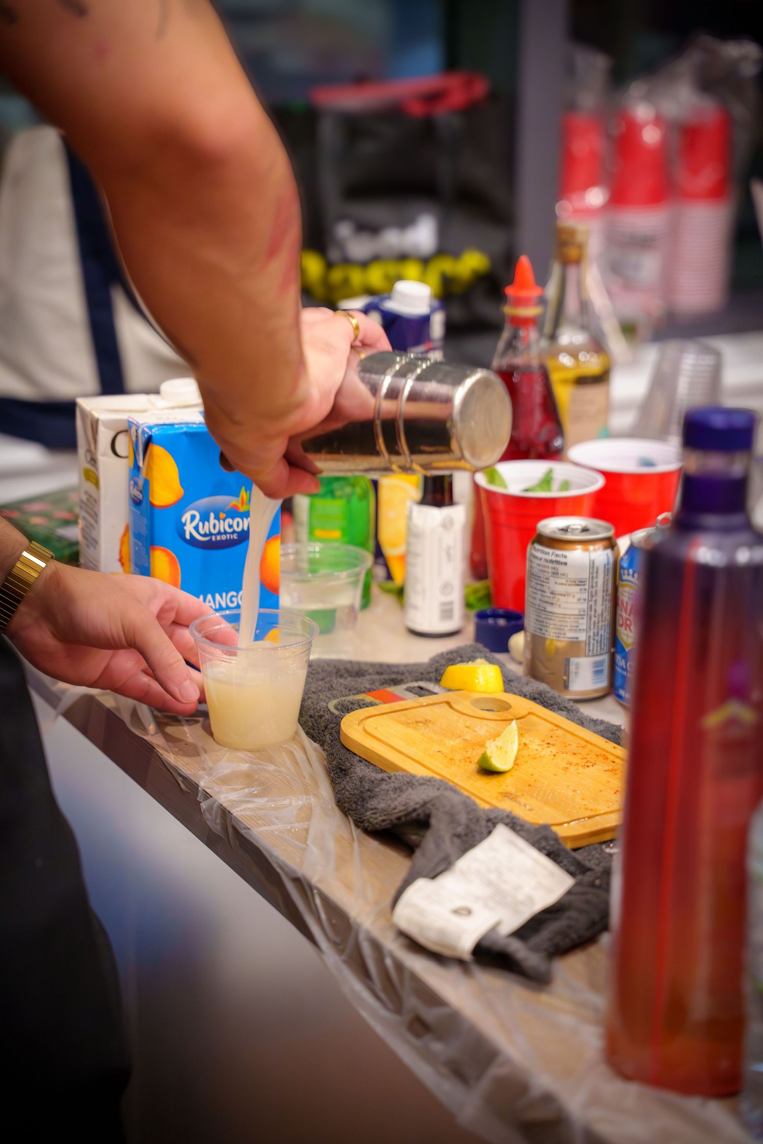 Close-up of drink preparation with various mixers and ingredients on a wooden cutting board.