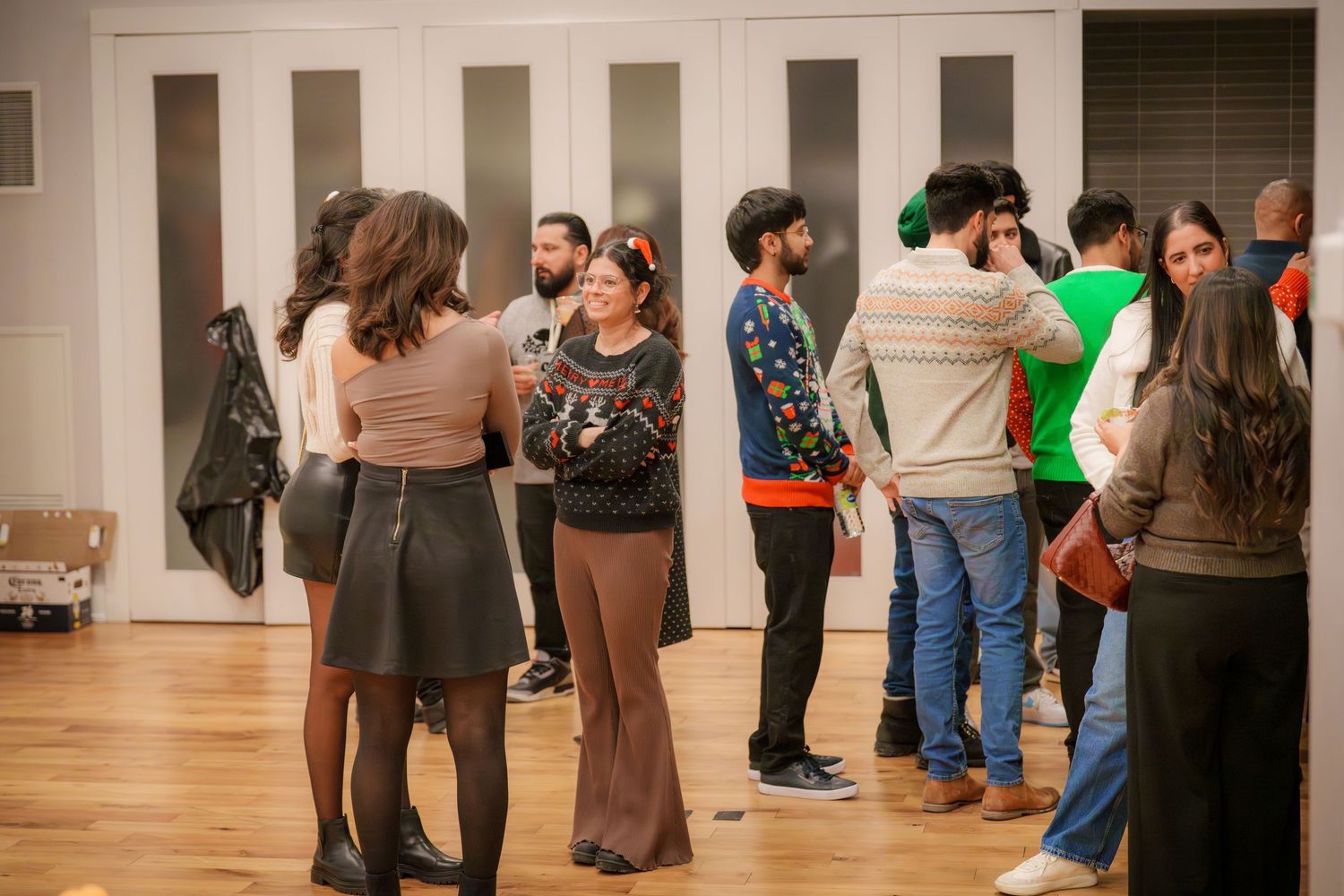 Wide shot of people mingling in a spacious room with wooden floors.
