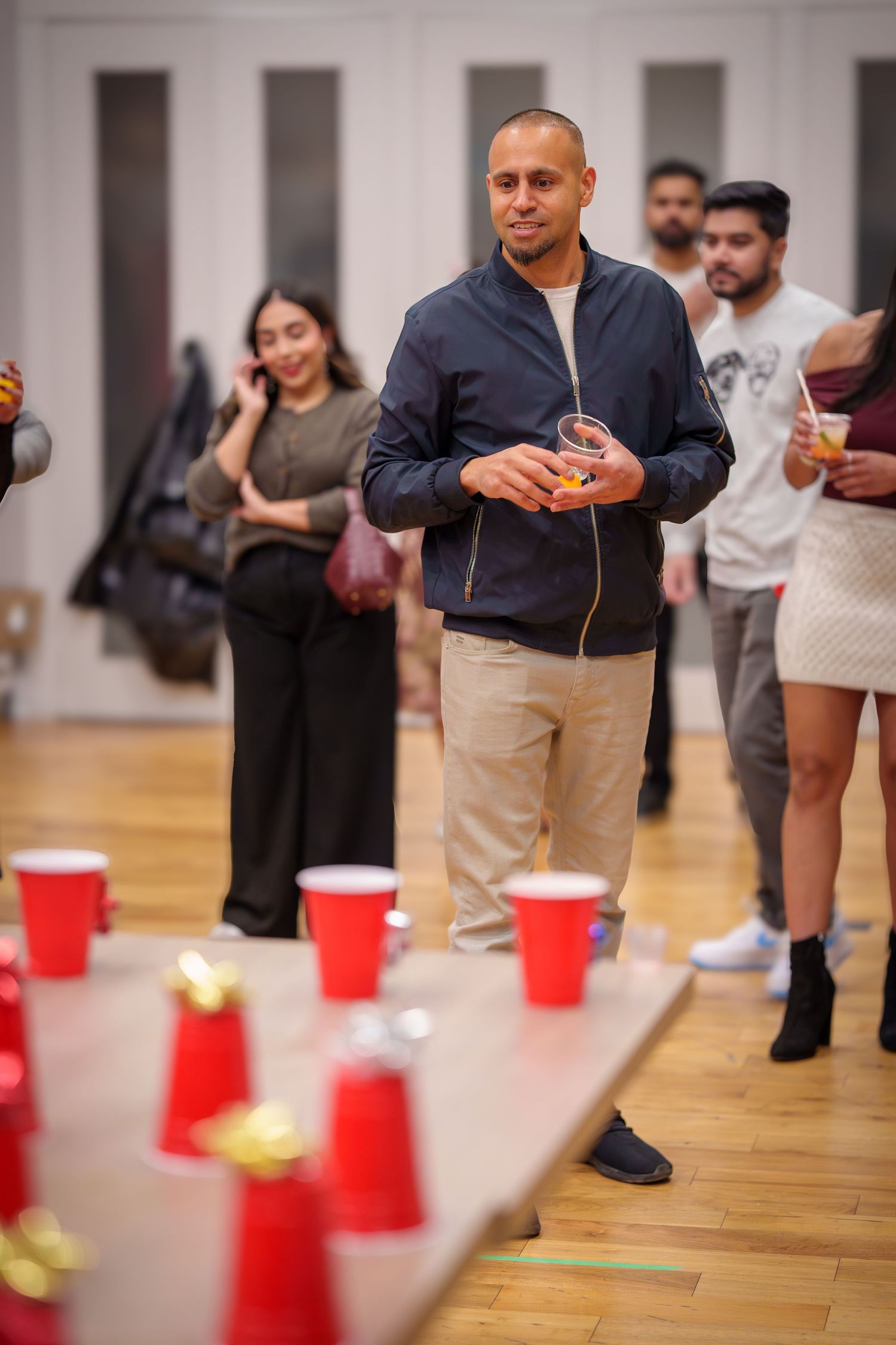 People playing a game with red plastic cups arranged on a wooden floor during a social gathering.