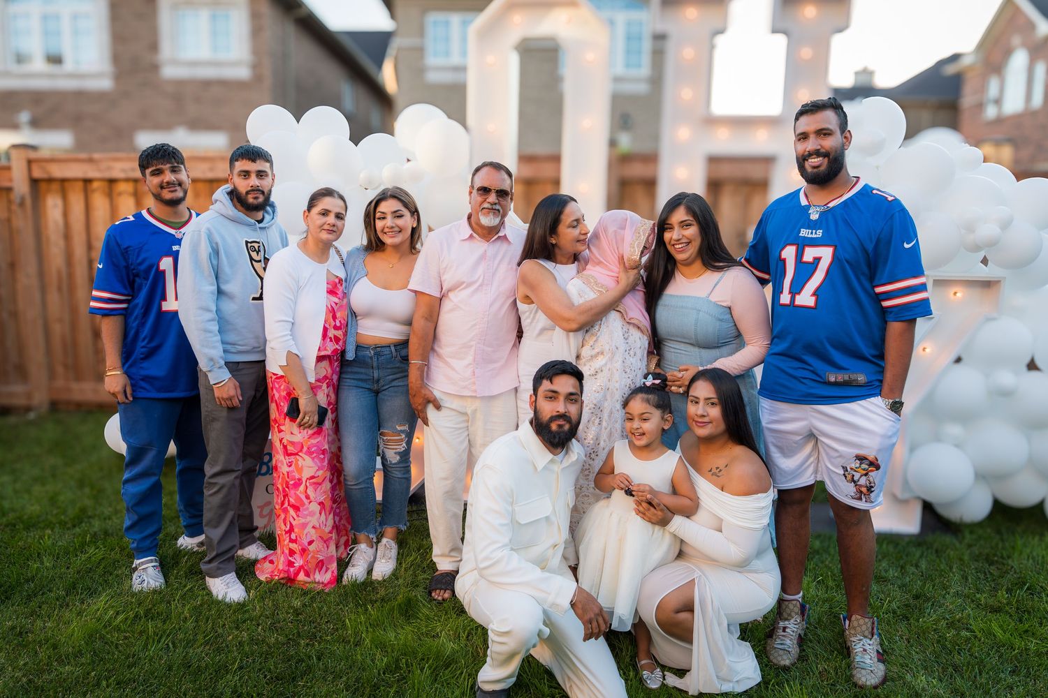Family group photo at a gender reveal party with white balloons, blue jerseys, and festive outdoor decorations.