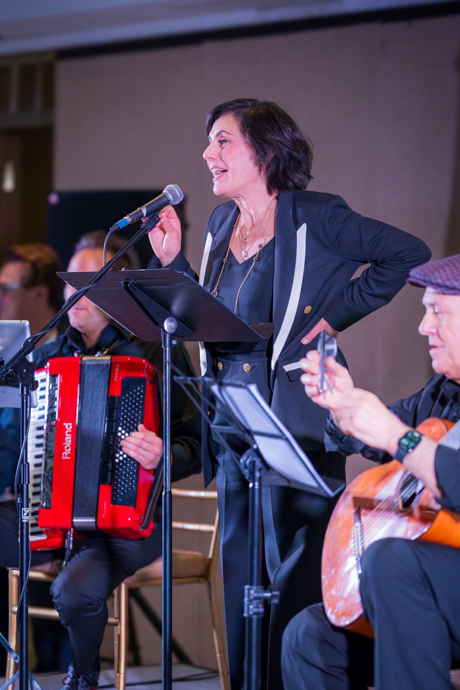 Woman in black jacket performs on stage with accordion and guitar musicians at live event.