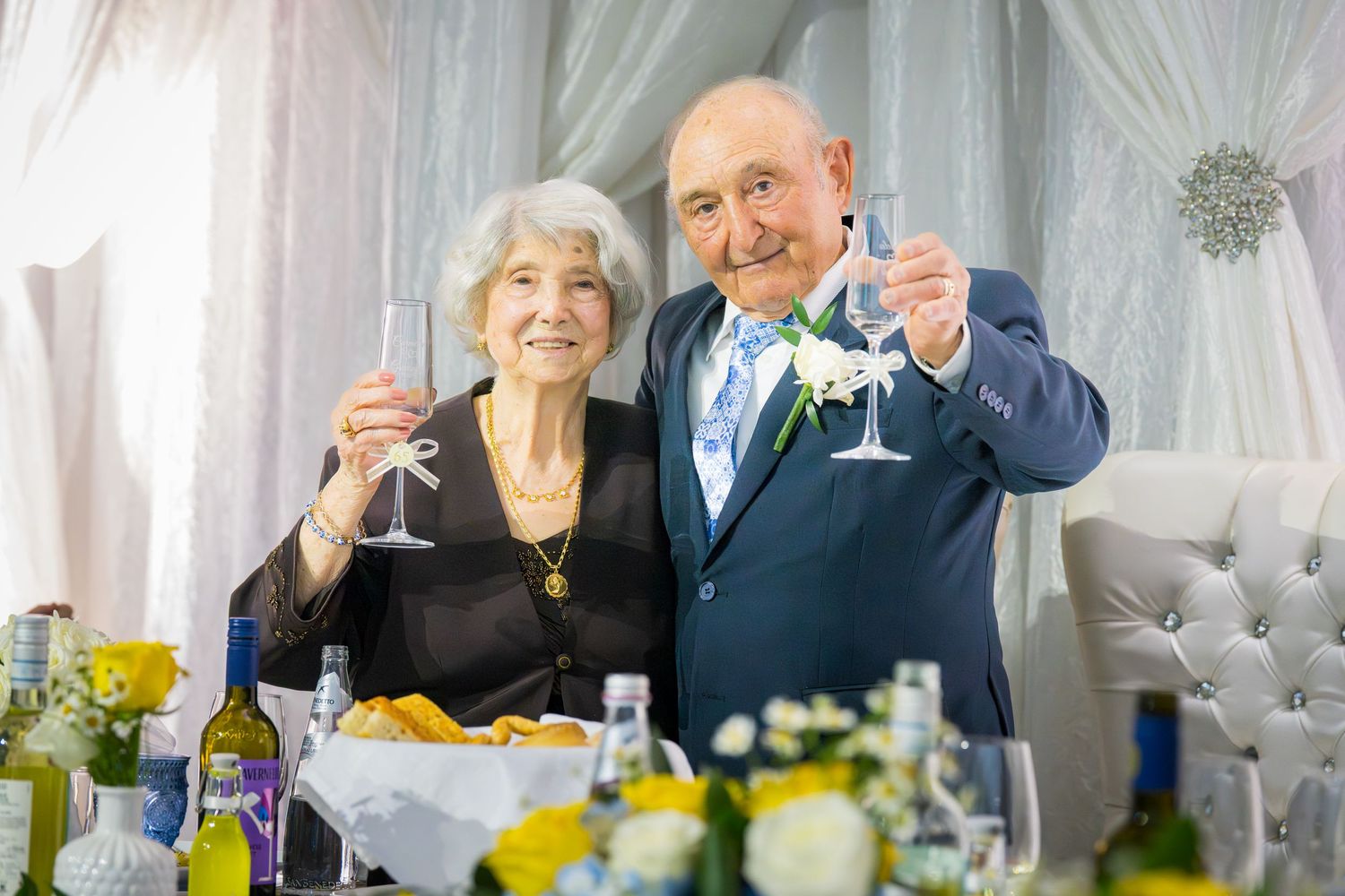 Elderly couple raising champagne glasses in a toast at an elegant wedding anniversary celebration.