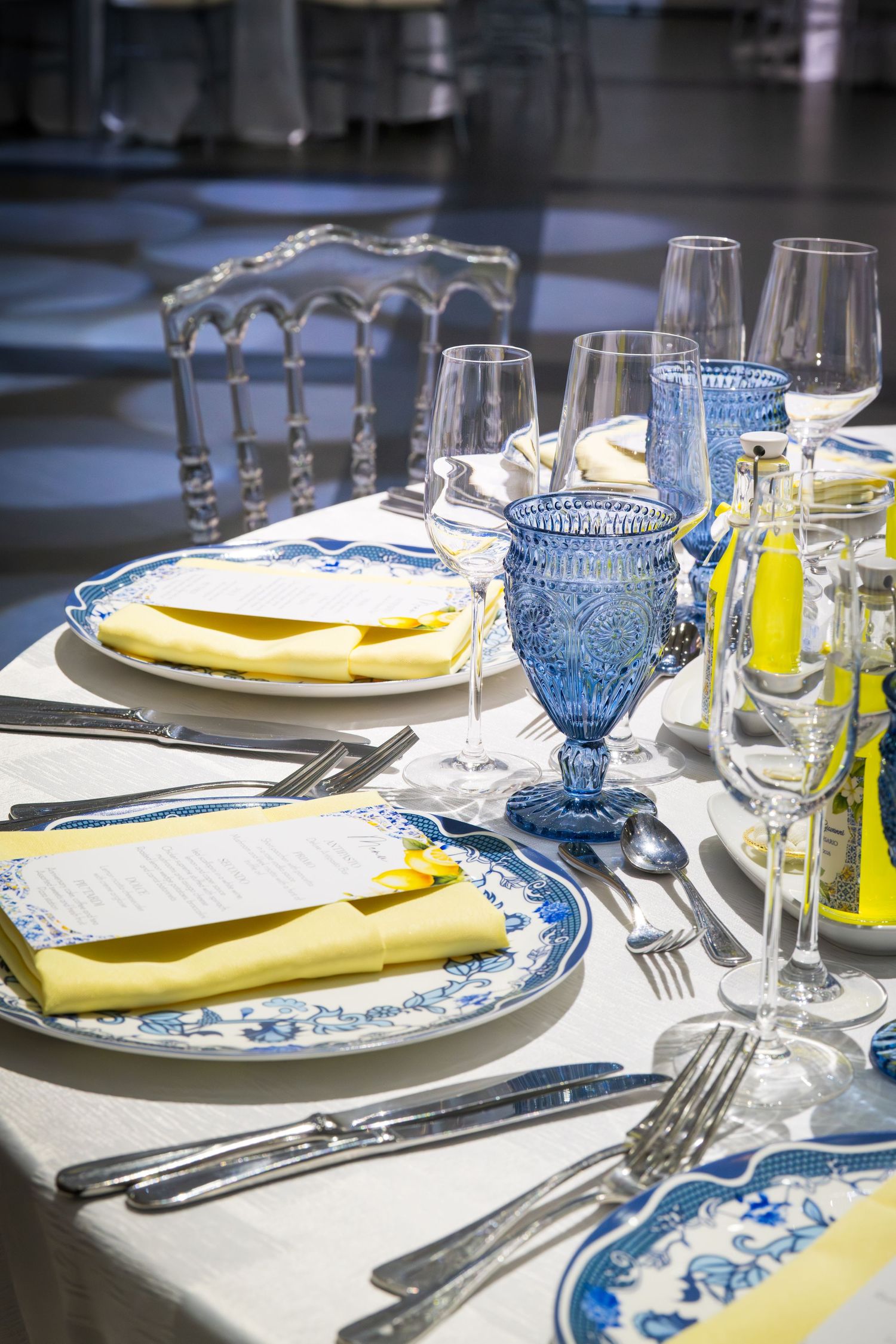 Elegant table setting with blue and white plates, yellow napkins, crystal glasses, and silverware for a formal event.