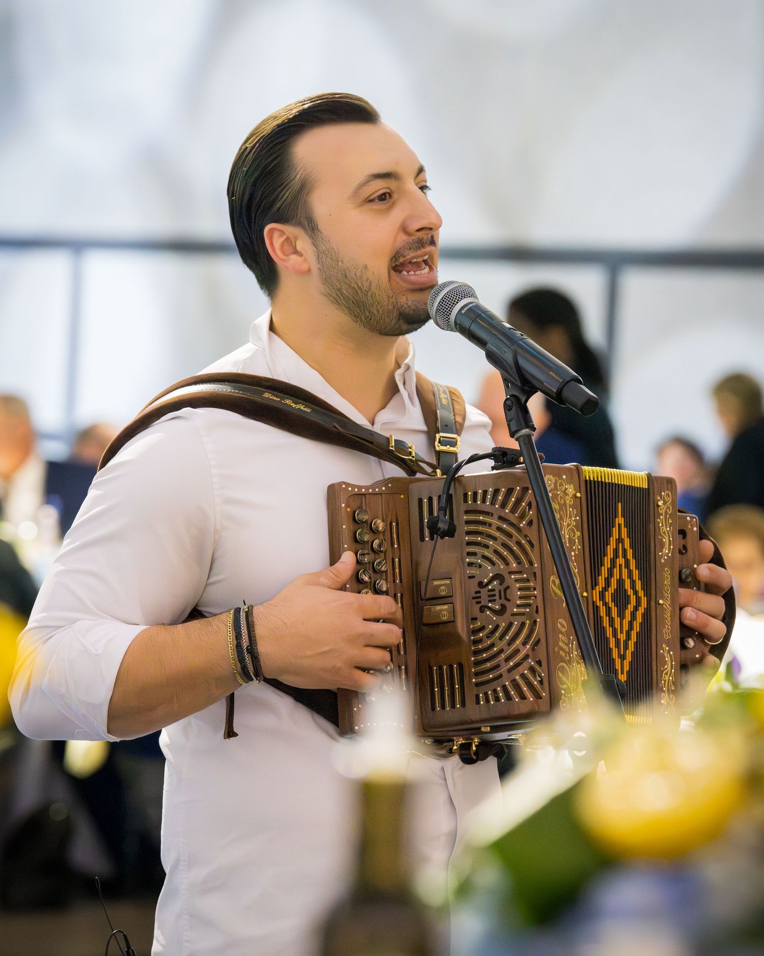 Close-up of male performer singing into microphone while playing decorative wooden accordion at festive event.