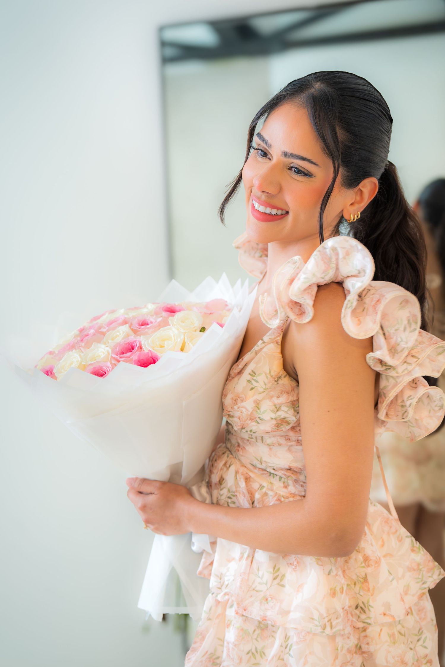 Young woman in floral dress smiling while holding large bouquet of pink and white roses.