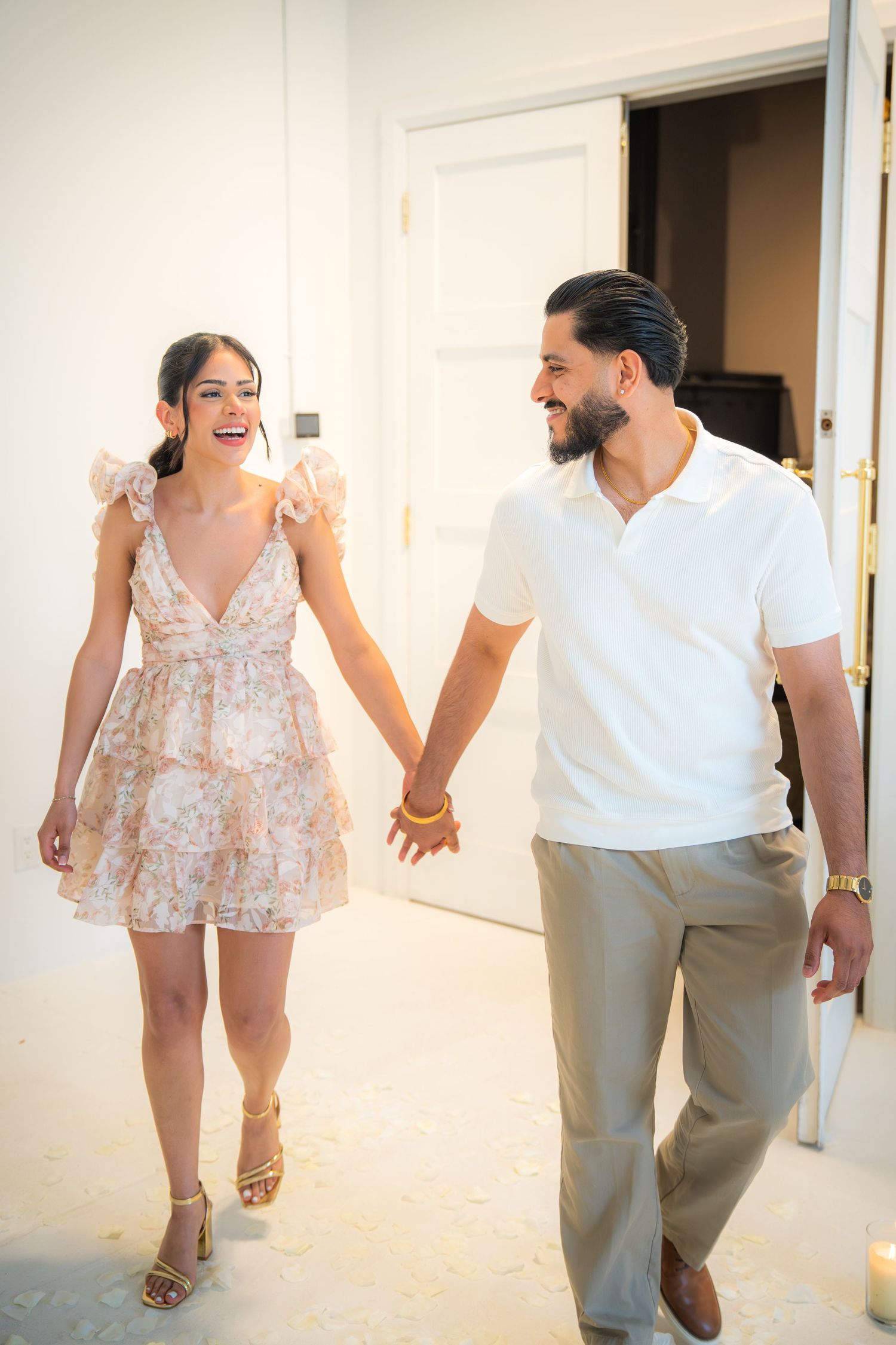 Happy couple holding hands walking together, woman in floral mini dress and man in white polo shirt.