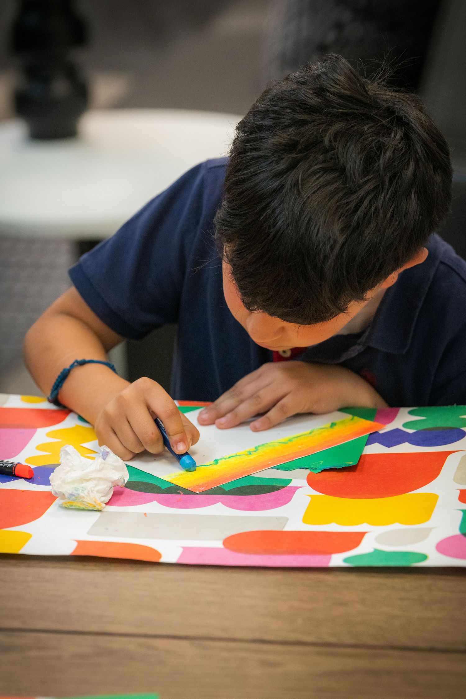 Young boy in navy polo shirt concentrates while drawing with blue marker on colorful art project.