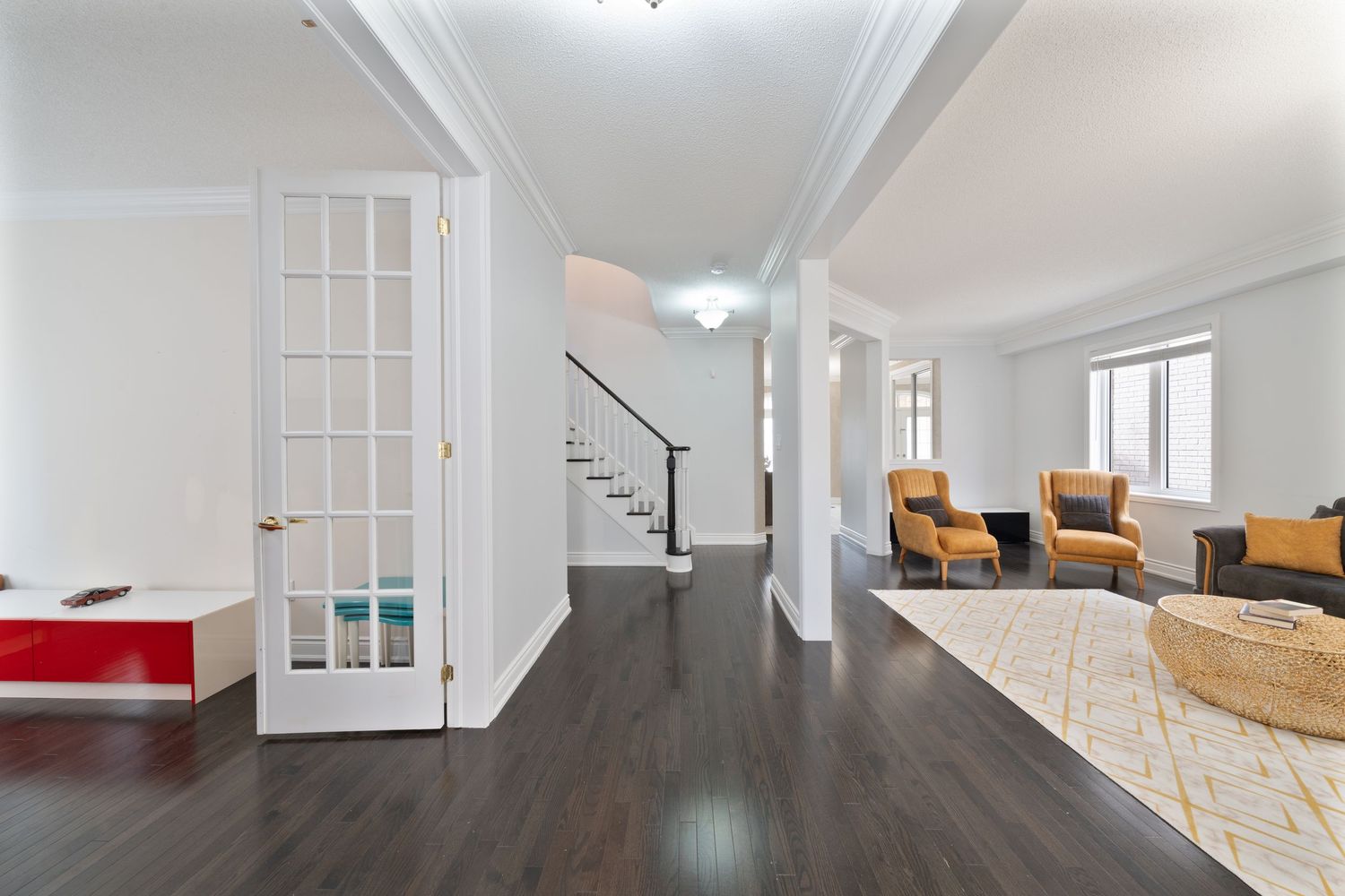 Modern white interior room with hardwood floors, crown molding, and natural light streaming through French doors.