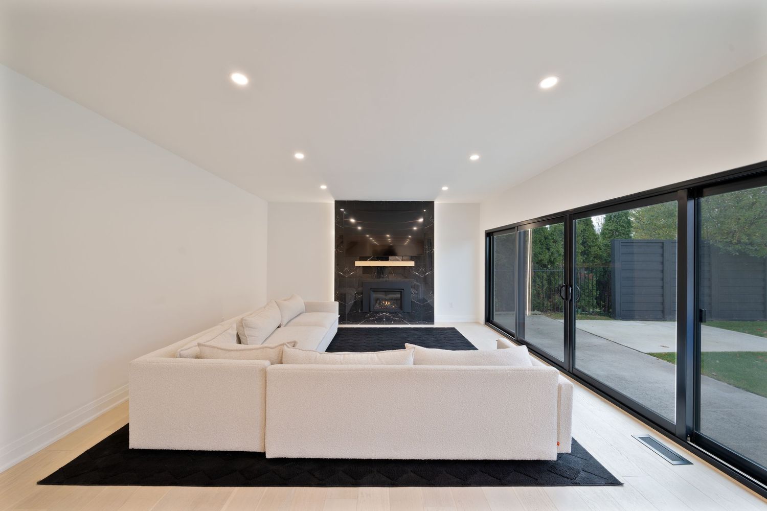 Modern white kitchen with black countertops features sleek recessed lighting and large windows for natural illumination.