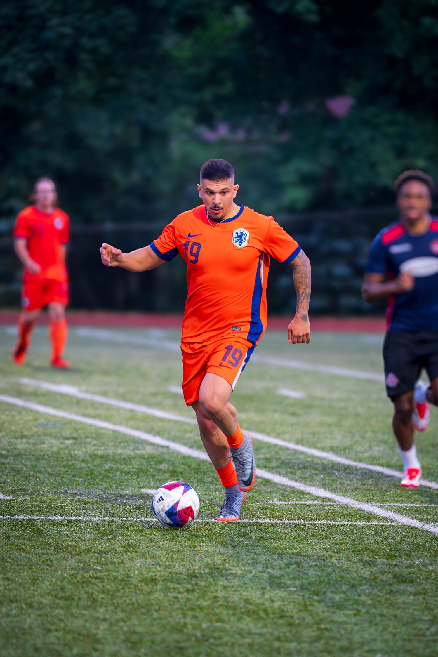 Player in orange uniform takes shot during soccer match on grass pitch.