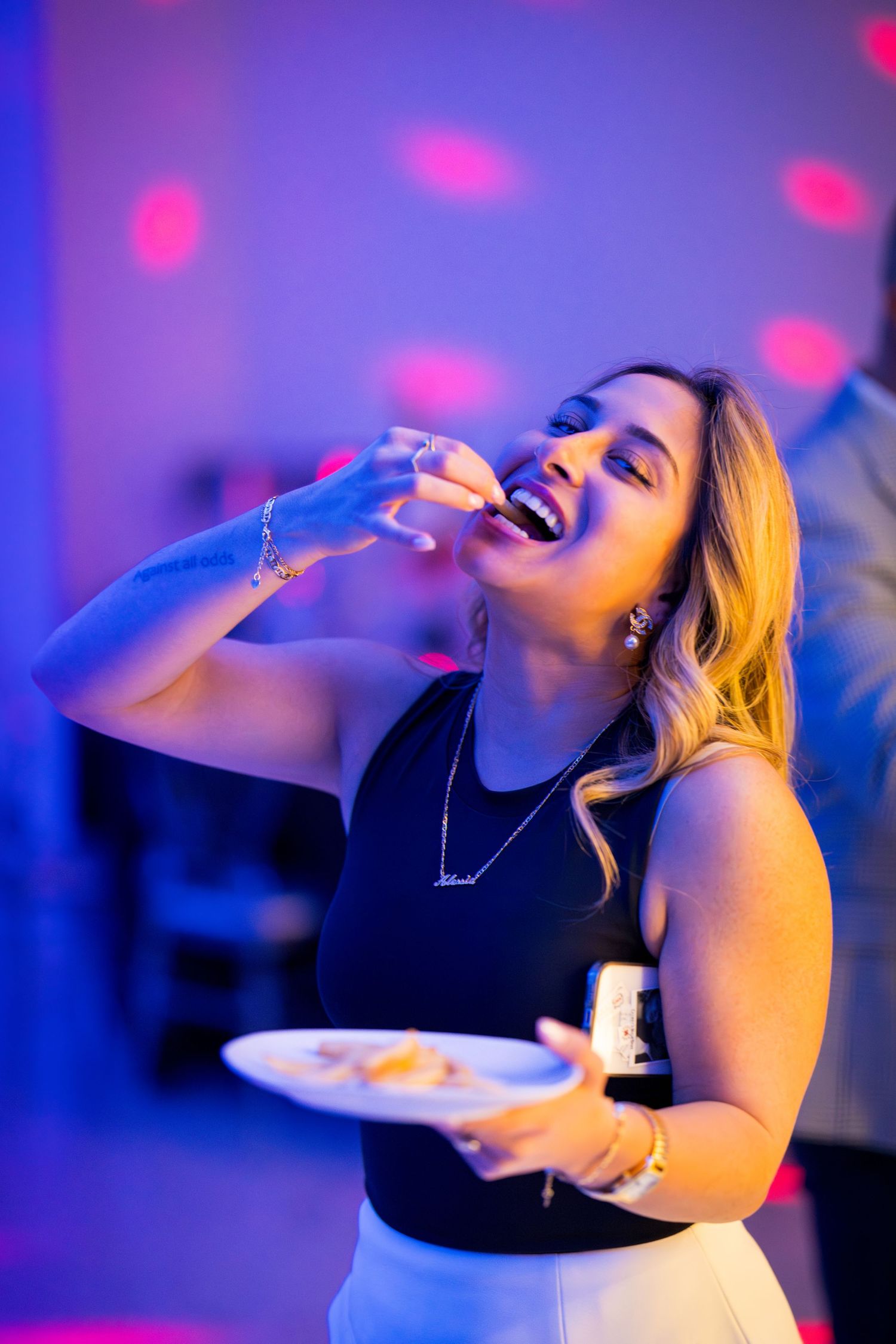 Person enjoying food and laughing at a party with purple and blue mood lighting.