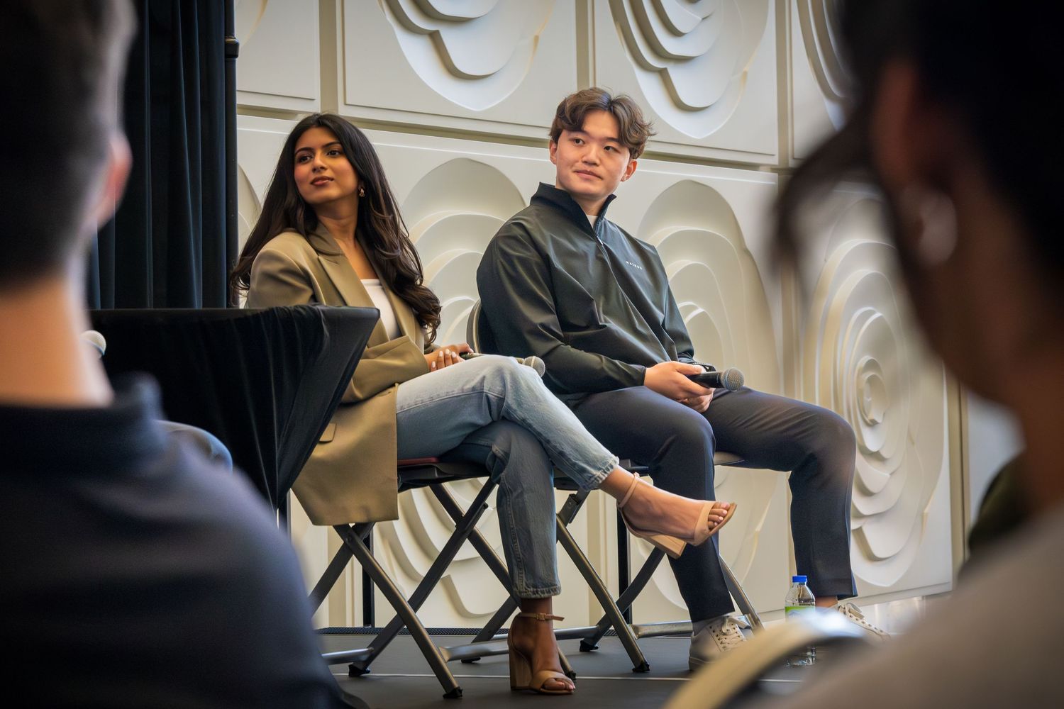 Side view of panel discussion with speakers seated on folding chairs against textured wall.