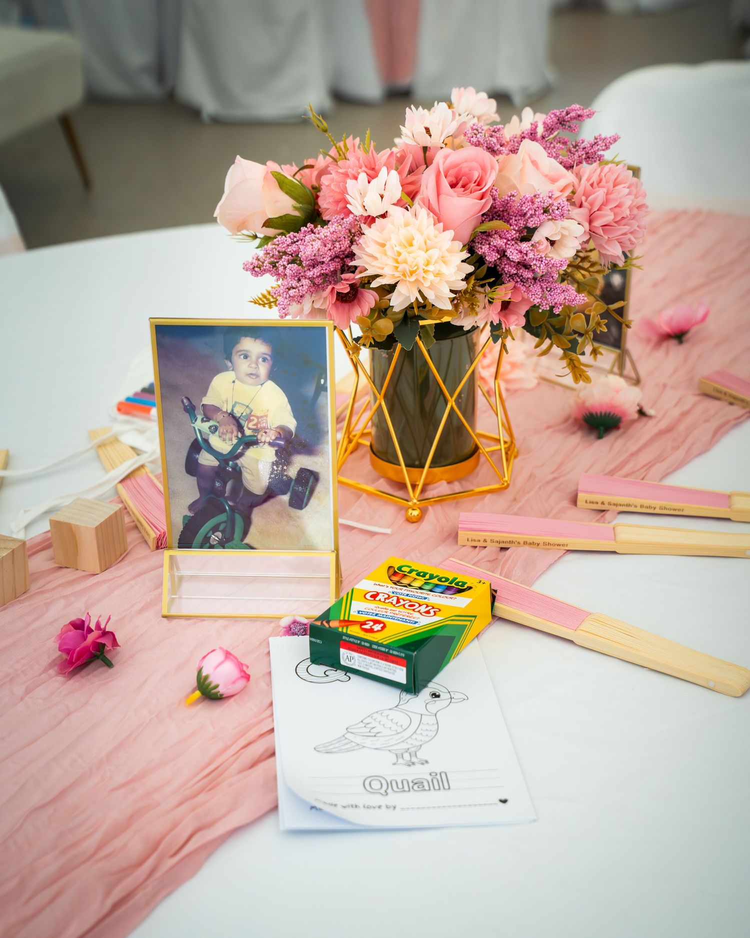 Pink floral centerpieces and coloring activities arranged on tables with gold accents and white linens.