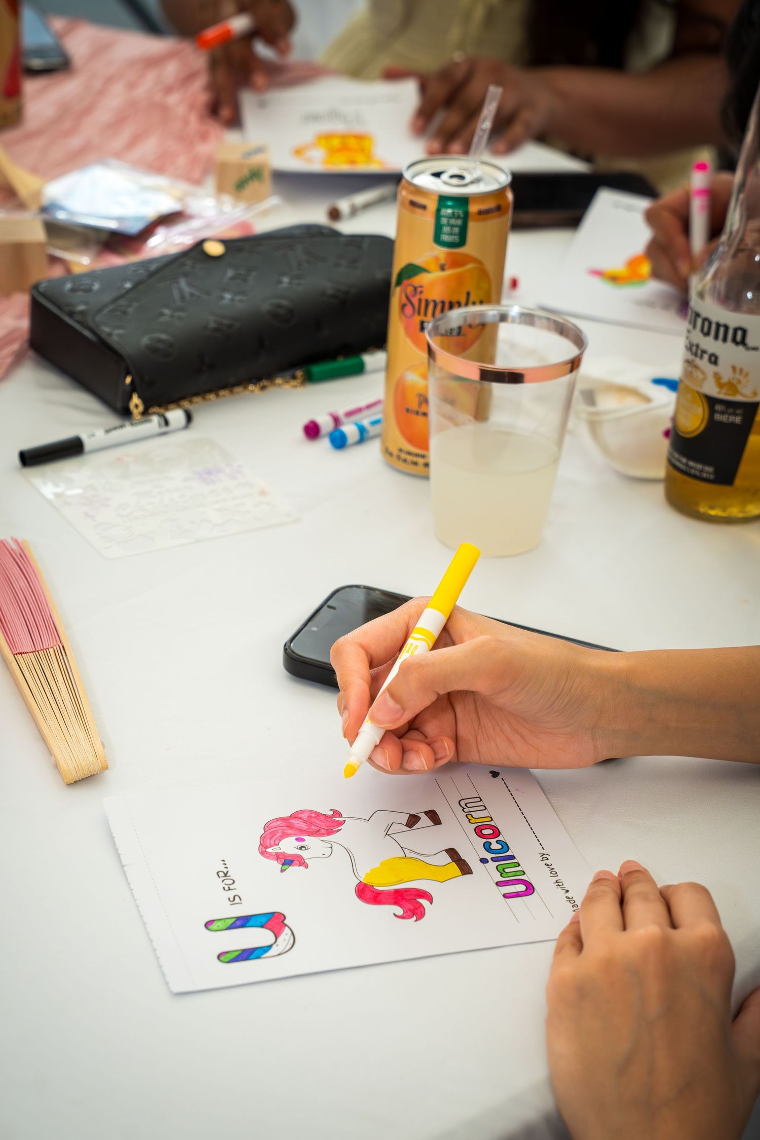 Hand drawing on a unicorn coloring page with drinks and supplies on table.