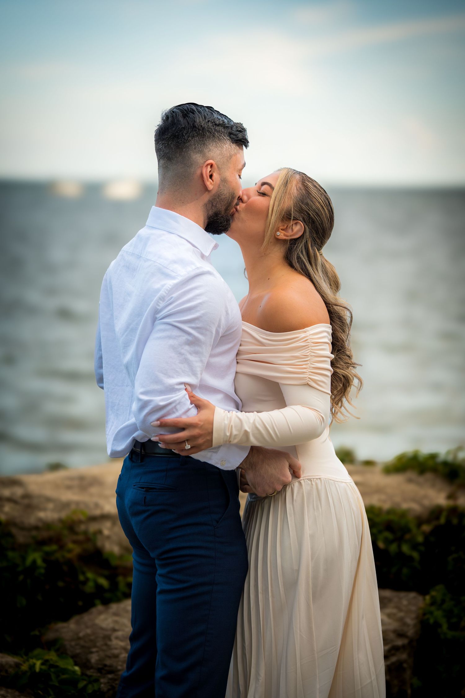 Romantic seaside moment between couple in formal attire against ocean backdrop.