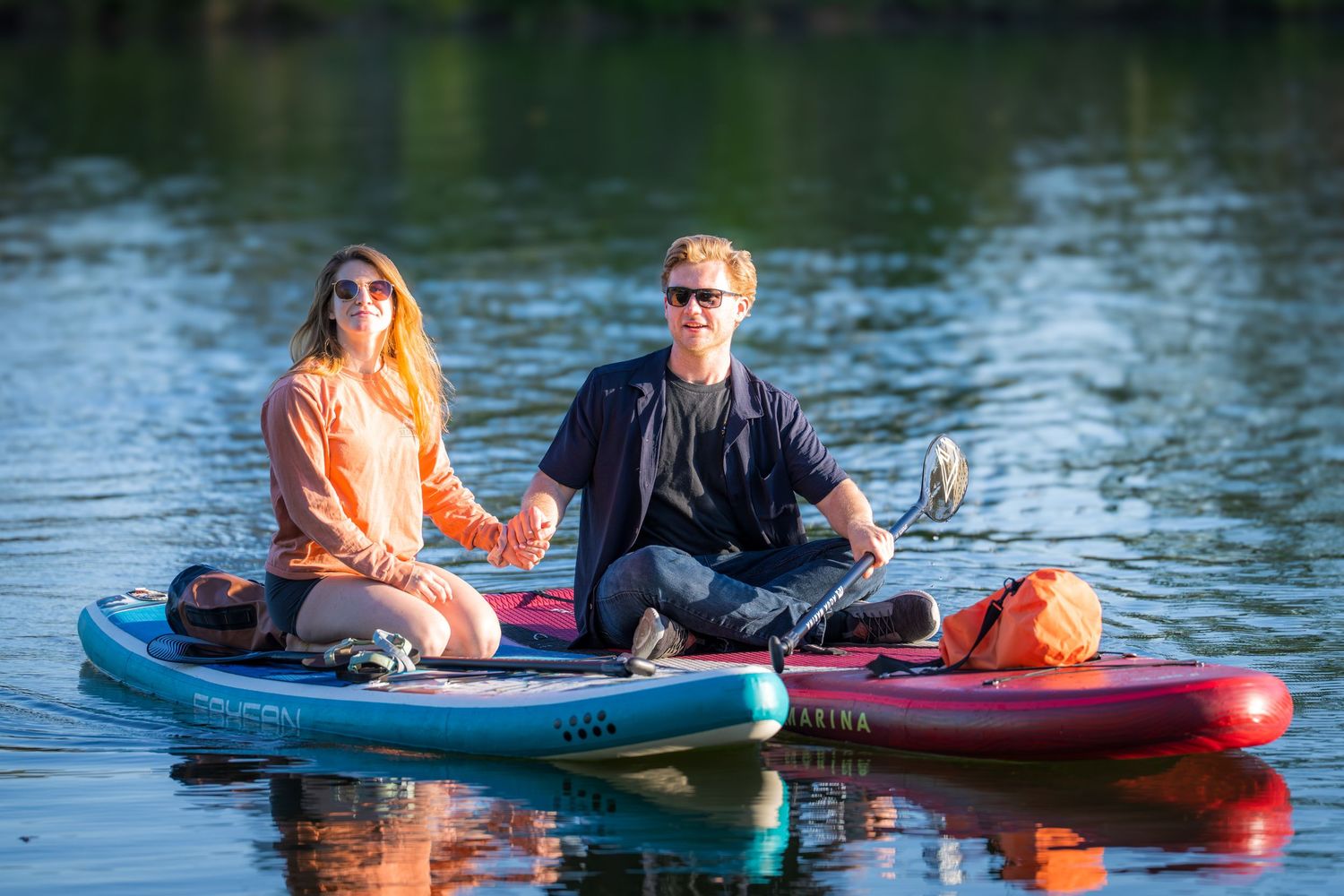Couple sitting together on paddleboards on a calm reflective lake during golden hour.