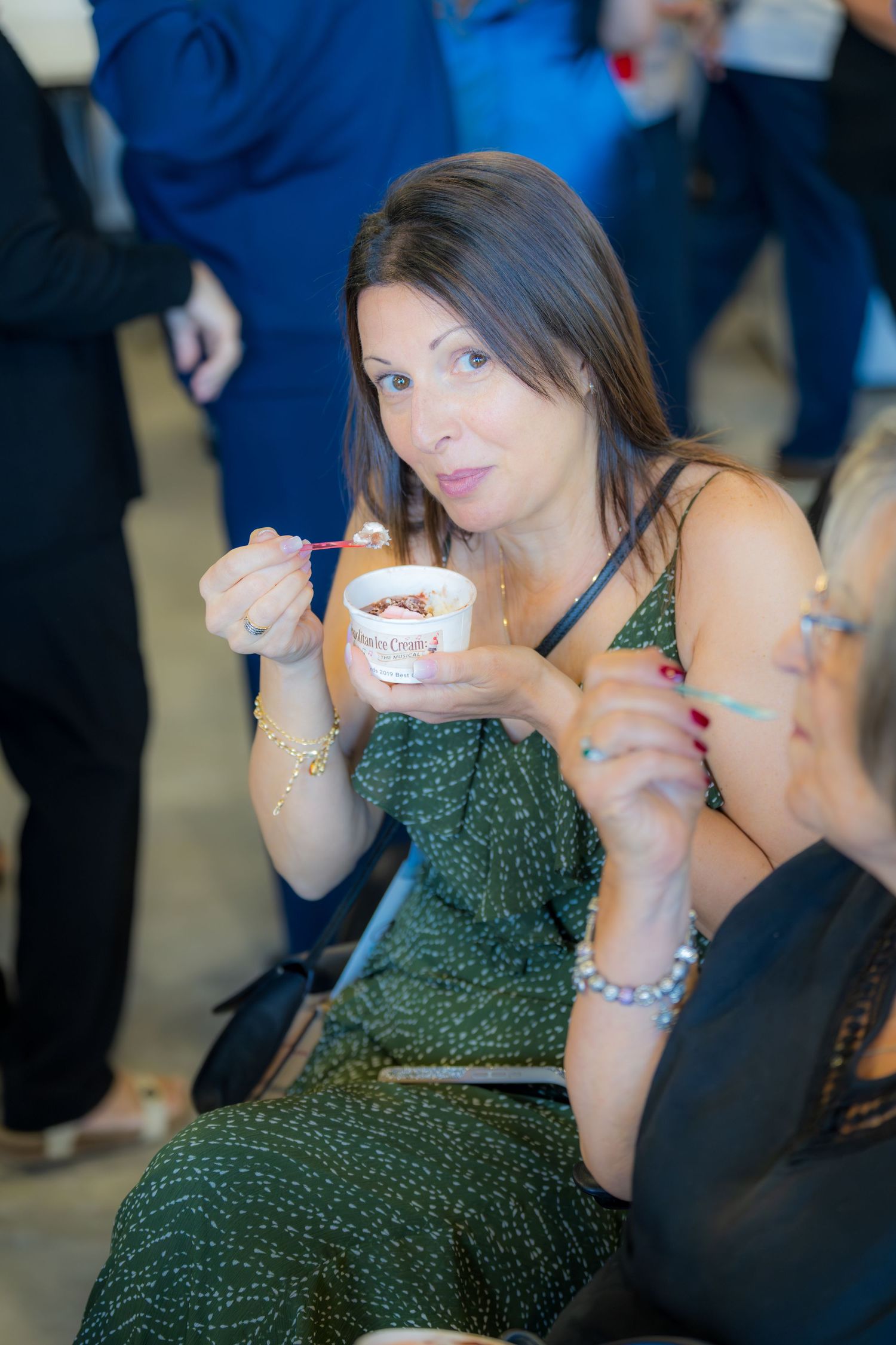 Dark-haired woman eating Haagen-Dazs ice cream cup at an indoor event.