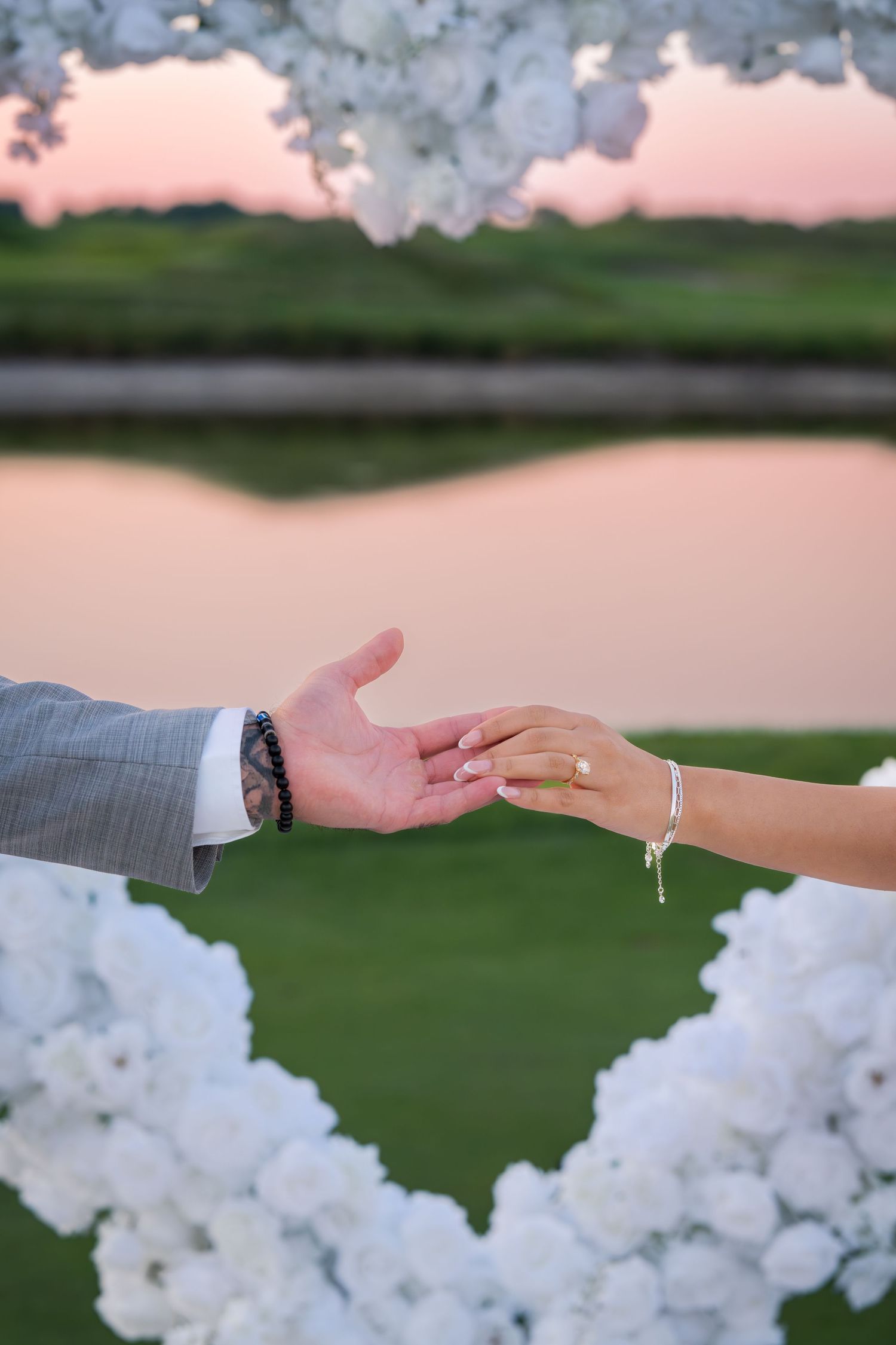 Hands reaching towards each other with white balloon arch and sunset backdrop.