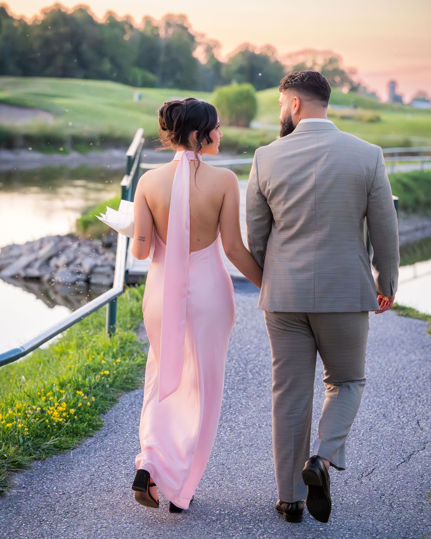 A couple in pink and gray attire walking together on a path during sunset at a golf course.