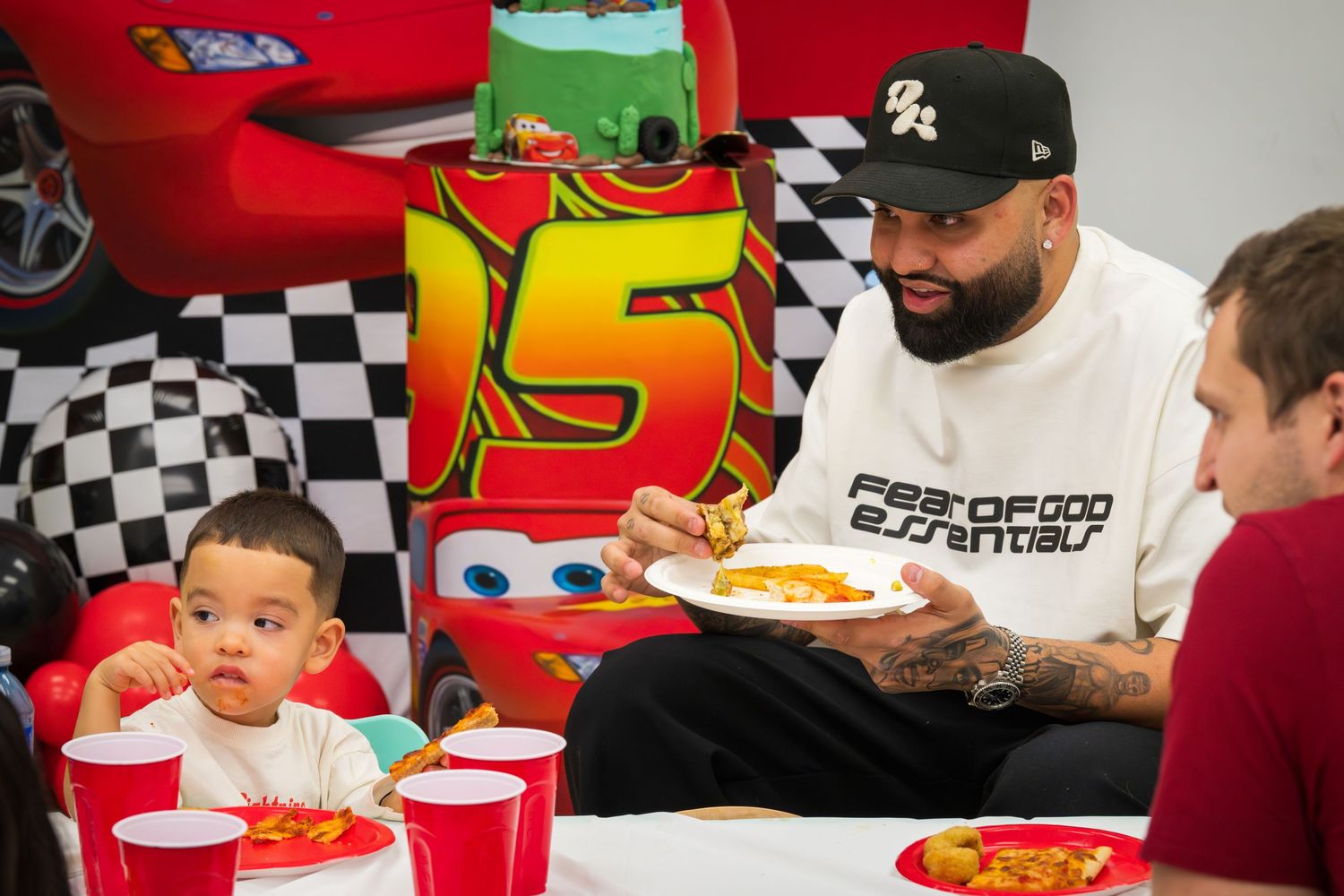 Toddler and bearded man eating at a Lightning McQueen Cars themed birthday party table.