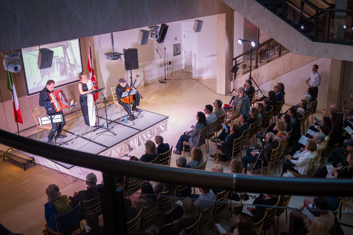 Aerial view of a live chamber music performance with audience seated in a modern concert hall with flags on stage.