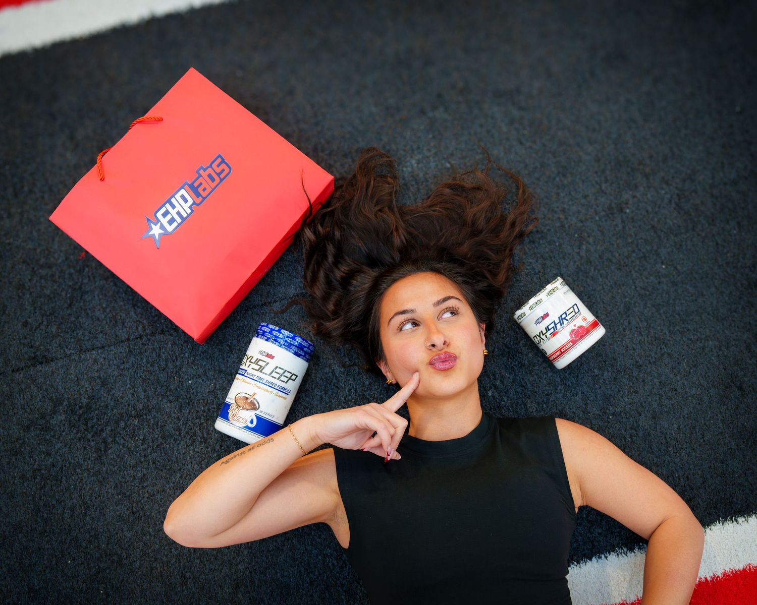 Woman lying on floor with GNC protein supplements and red shopping bag, thinking pose, fitness lifestyle.