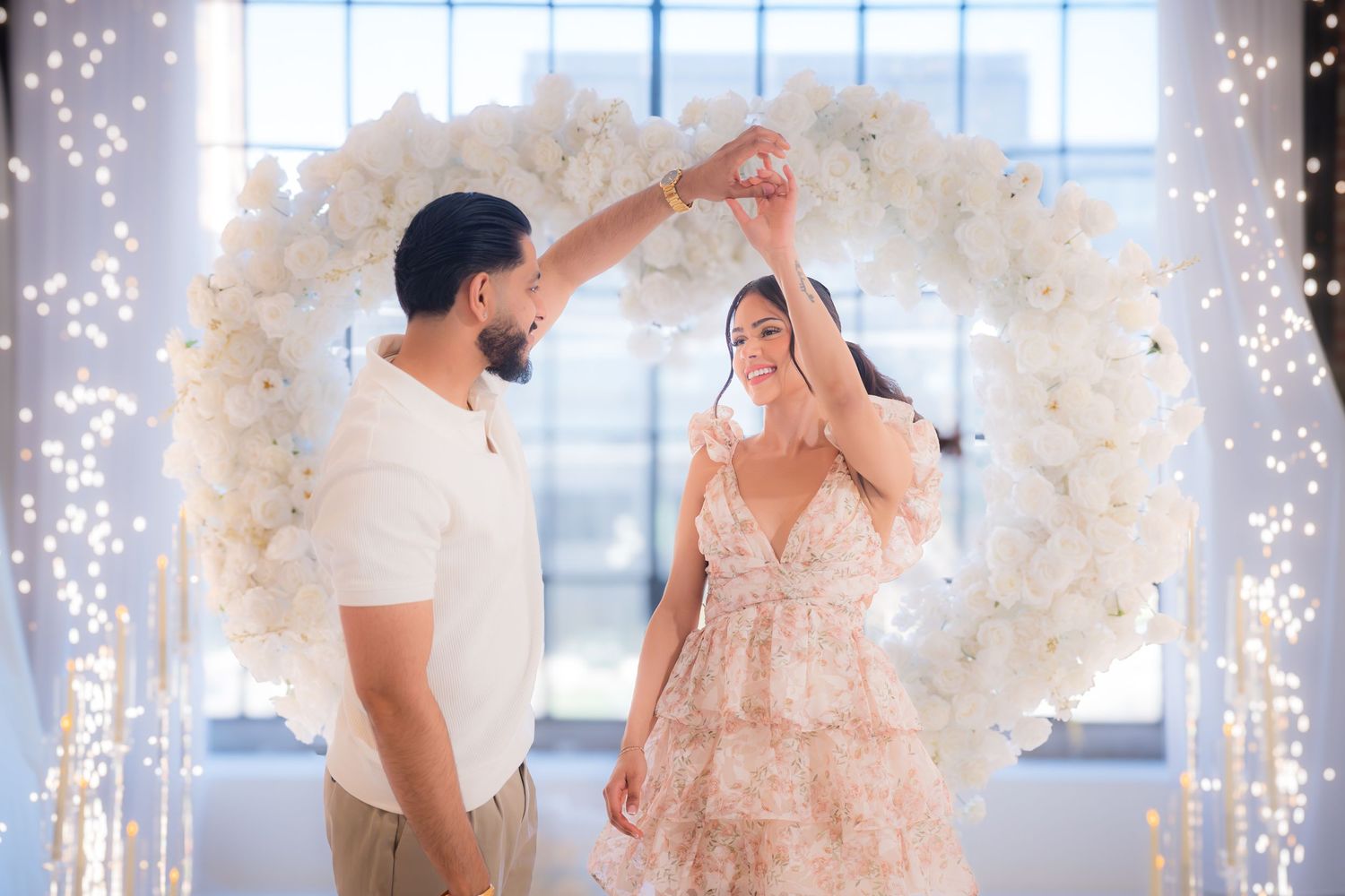 Couple dancing under a floral arch with fairy lights at a romantic wedding celebration.